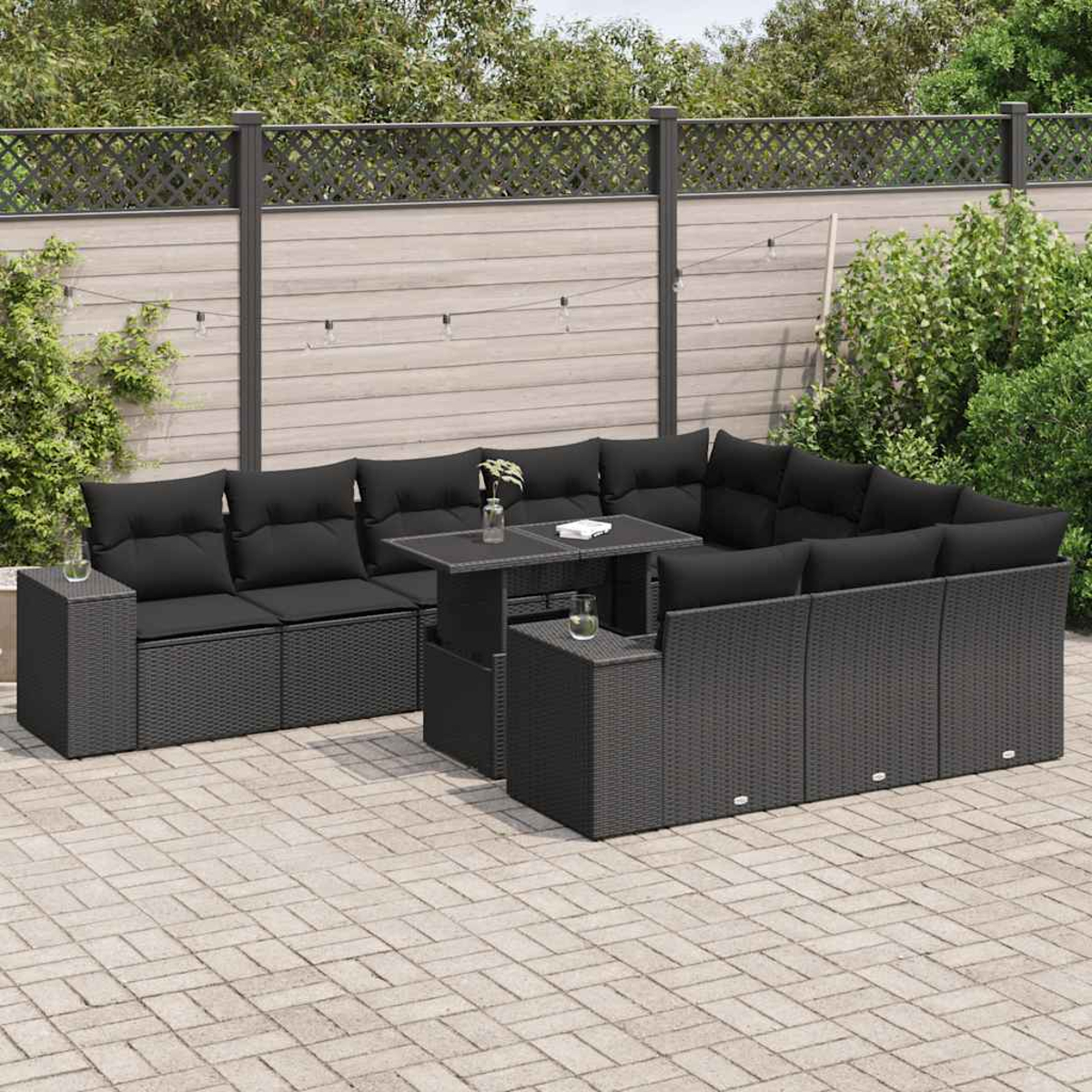 Un set da patio con cuscini neri, un tavolo e un patio in mattoni grigi con una staccionata in legno sullo sfondo.
