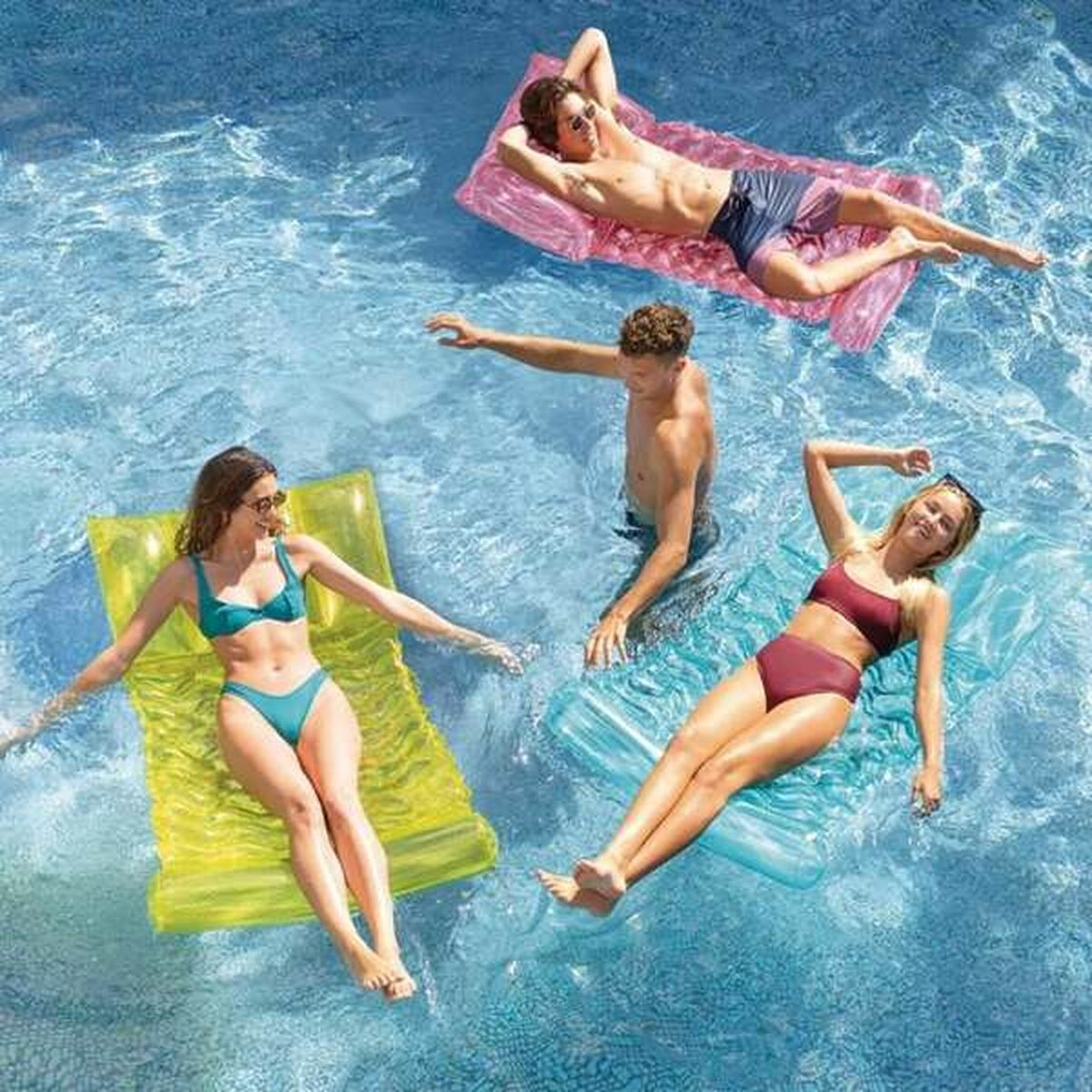 Menschen schweben auf aufblasbaren Flößen in einem Pool. Das Wasser ist blau und die Sonne scheint.