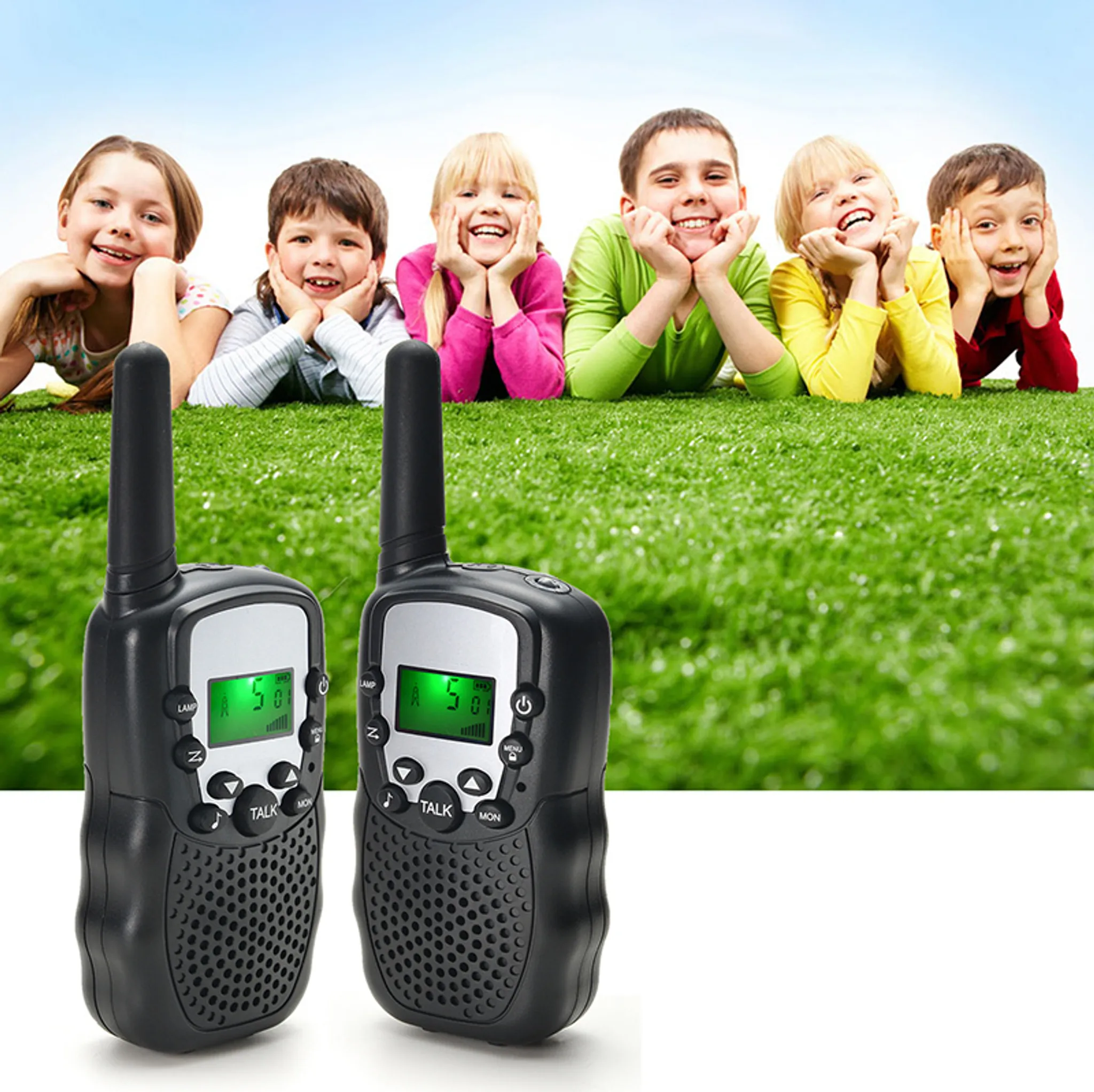 Zwei schwarze Walkie-Talkies auf grünem Gras. Sechs Kinder lächeln im Hintergrund und liegen.