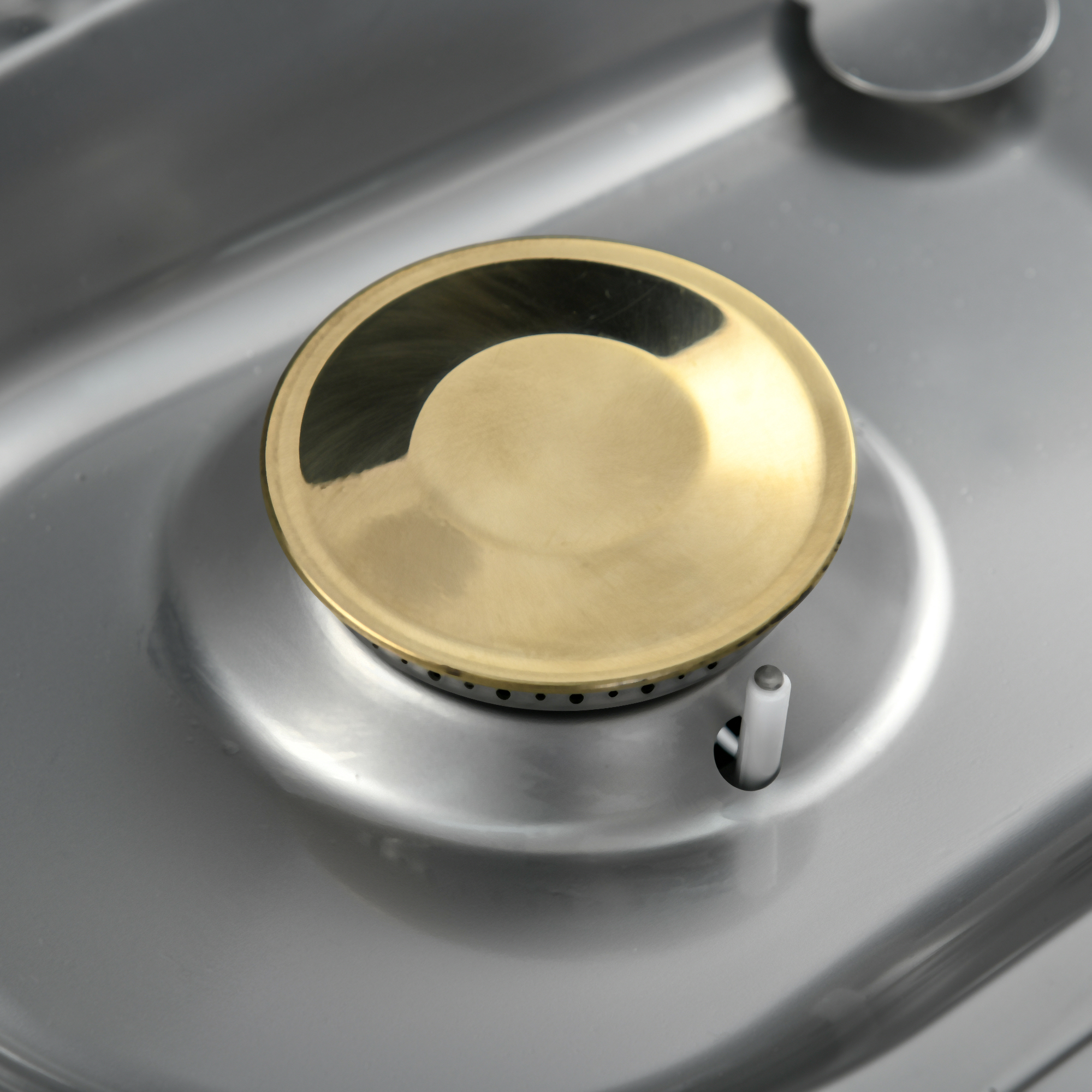 Nahaufnahme eines Metallbrenners auf einer Edelstahlfläche mit goldener Kappe.