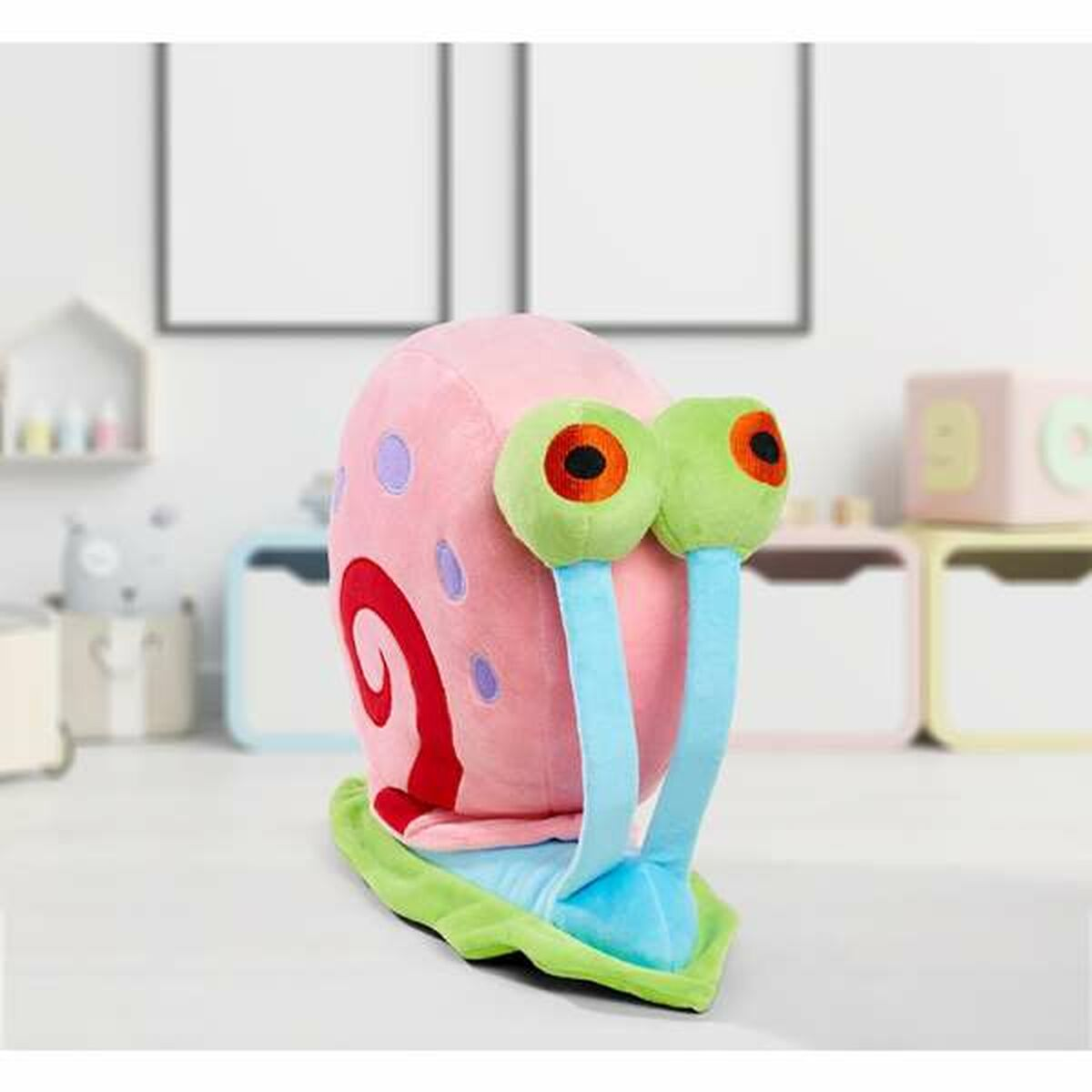 Peluche a forma di lumaca rosa con occhi verdi e base verde e blu, su superficie bianca.