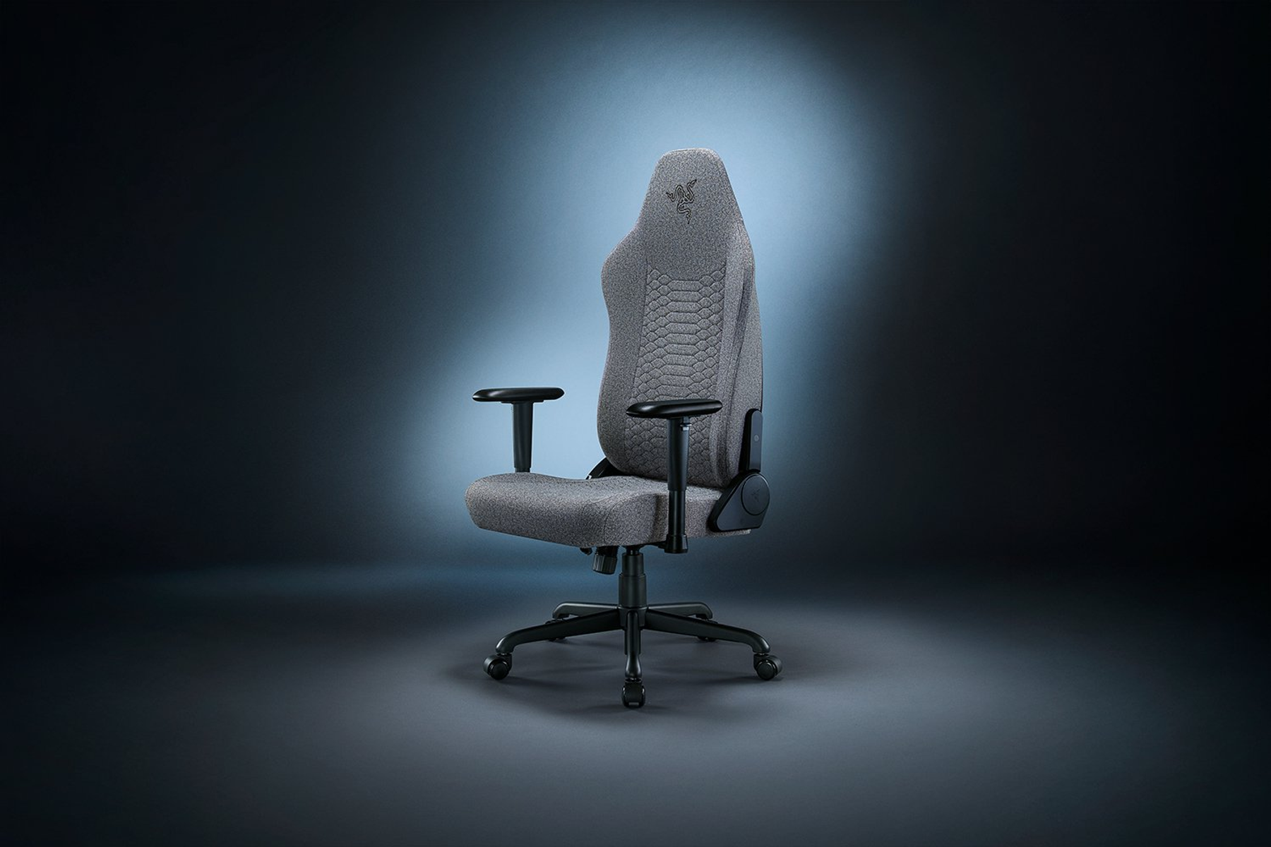 Koyu bir arka plan üzerinde gri Razer oyun koltuğu. Sandalye sola doğru eğiktir.