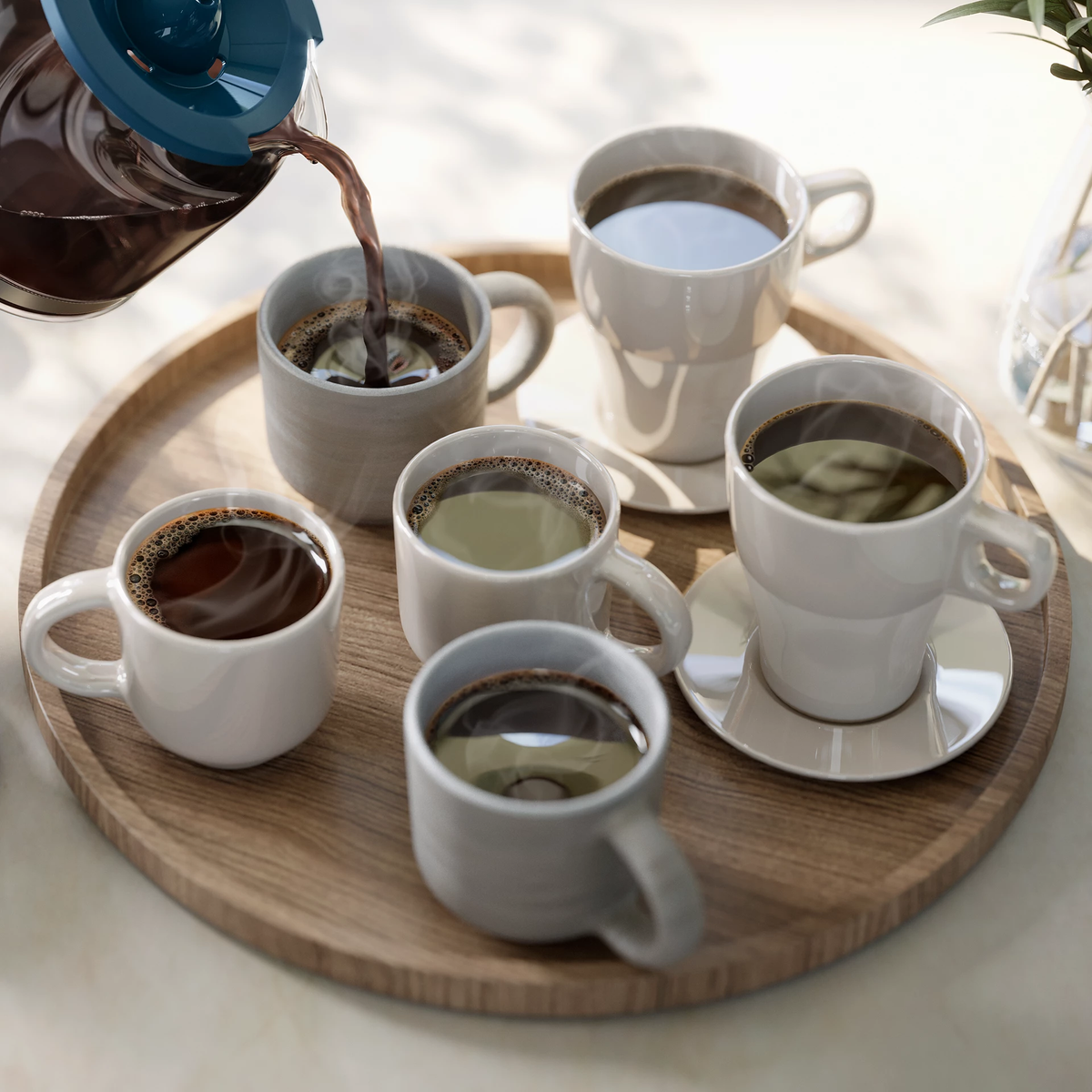 Kawa wlewana do wielu białych kubków na drewnianej tacy. Niektóre kubki mają spodki.
