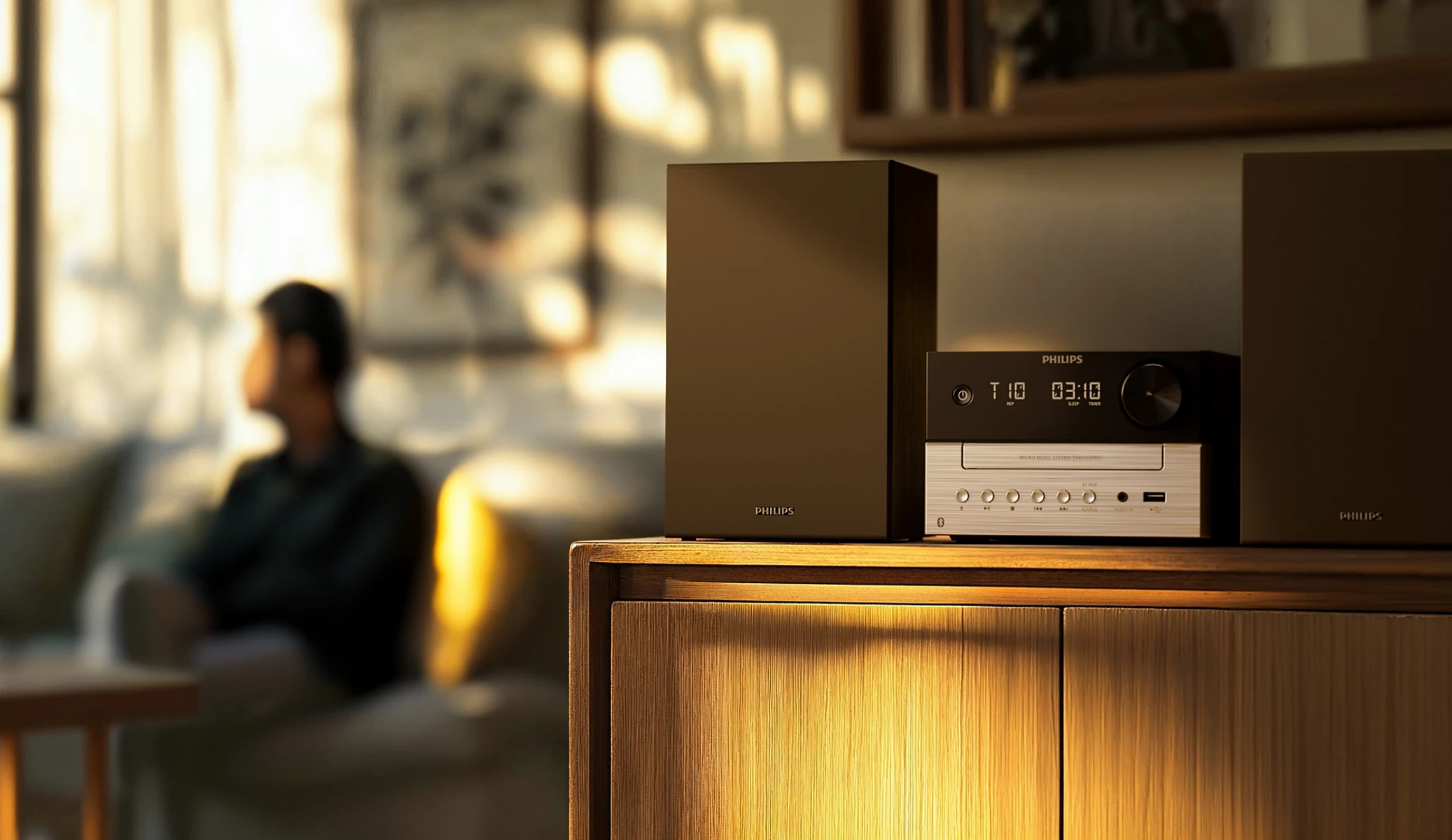 System stereo Philips na drewnianej szafce, z rozmytą osobą w tle.