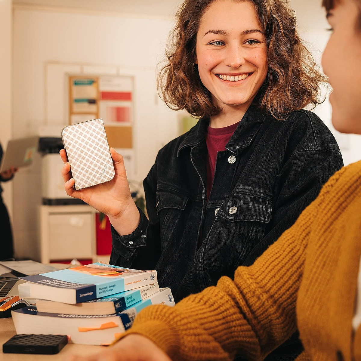 Kobieta trzymająca dysk twardy przed dwiema osobami, książki na pierwszym planie.