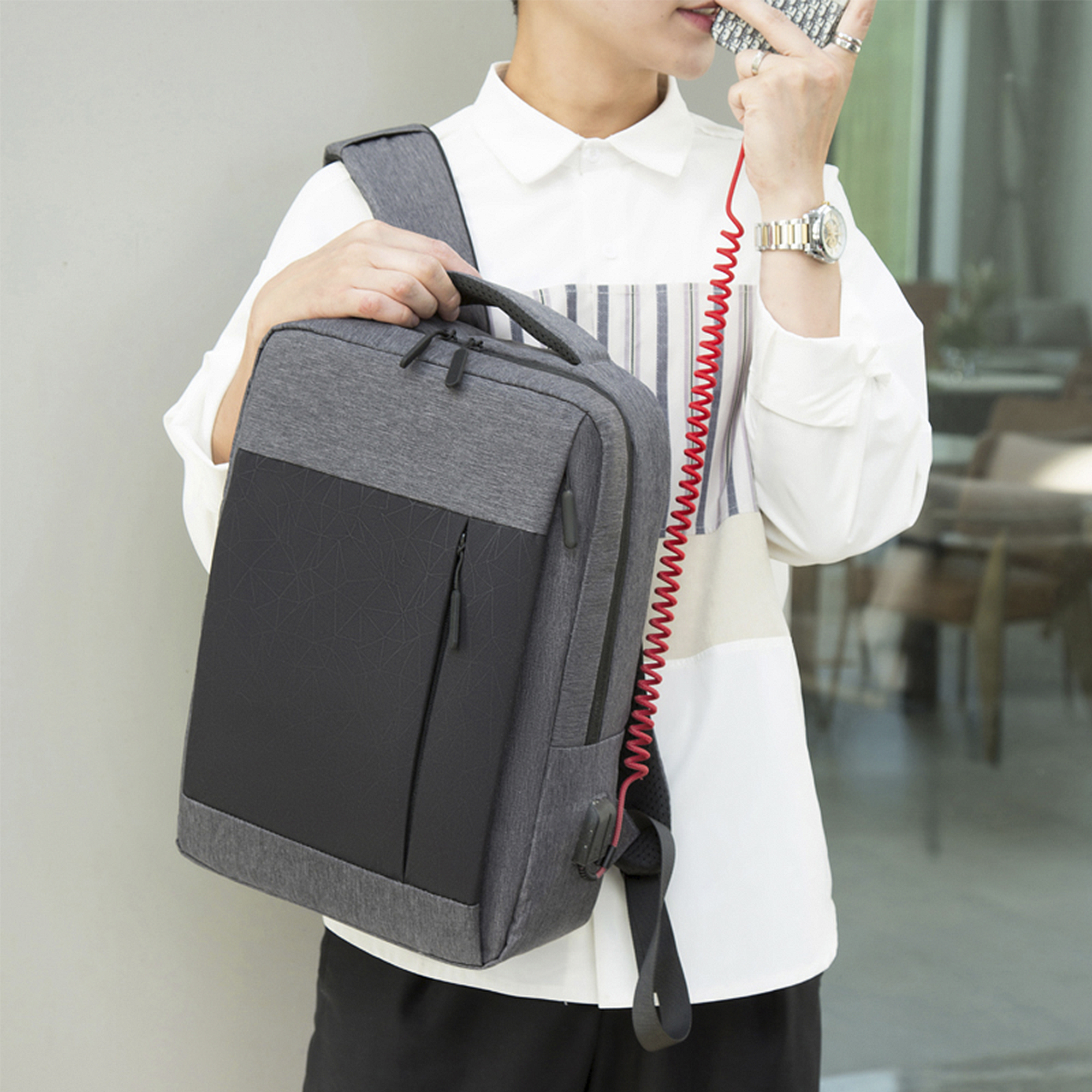 Una persona tiene un telefono, indossa uno zaino con un cavo rosso, su sfondo di camicia bianca.