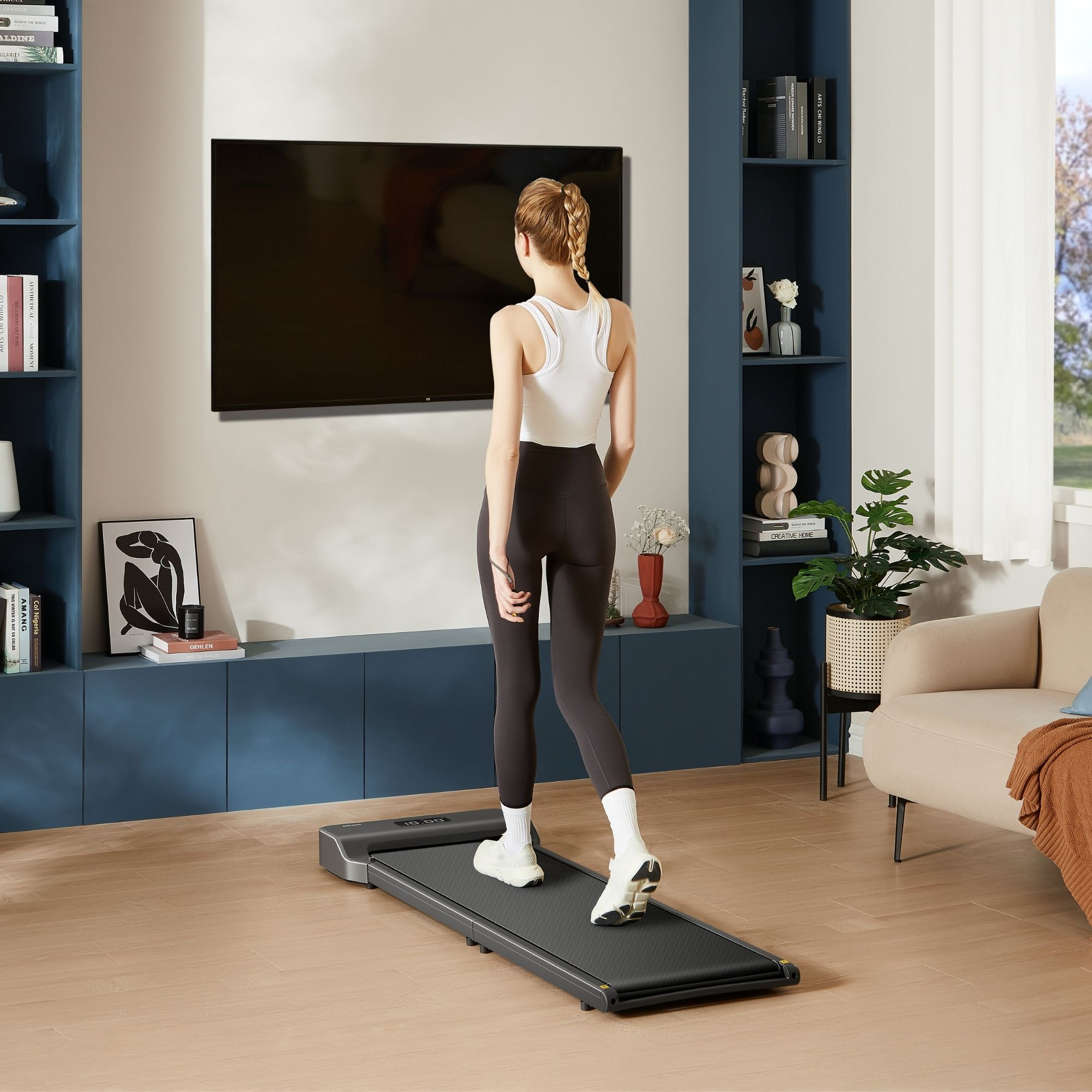 Mujer caminando en una cinta de correr en una sala de estar. TV y estanterías al fondo.