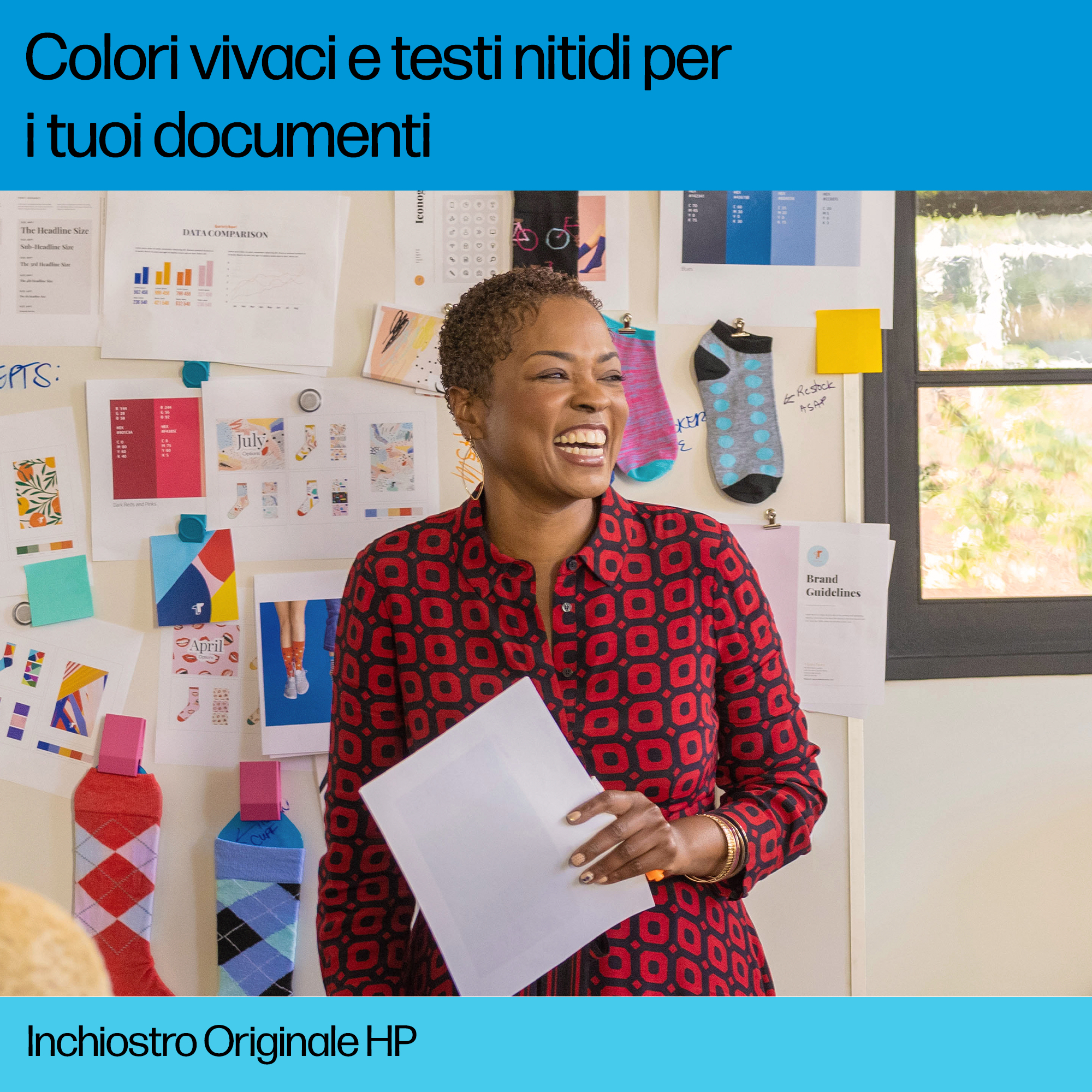 Una donna sorridente, che tiene un foglio, in una stanza con fogli colorati appesi al muro dietro di lei.