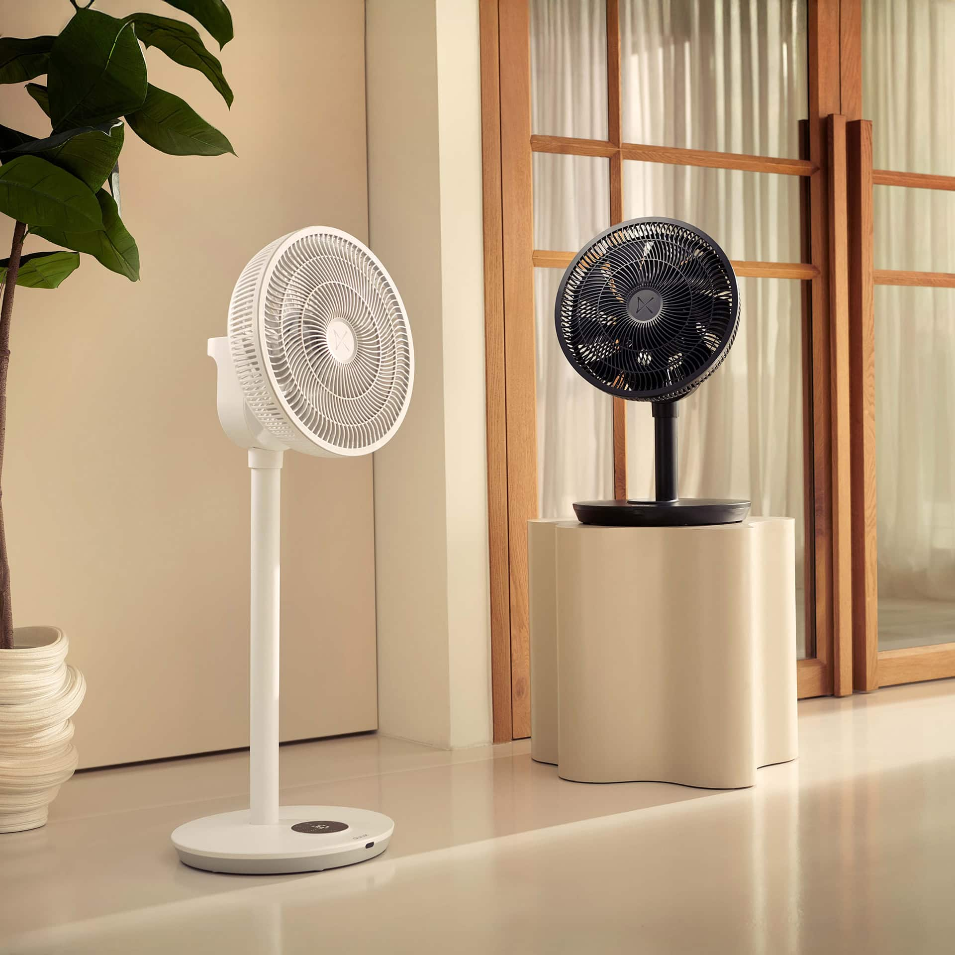 Twee staande ventilatoren in een kamer. Eén wit, één zwart, op een beige tafel.