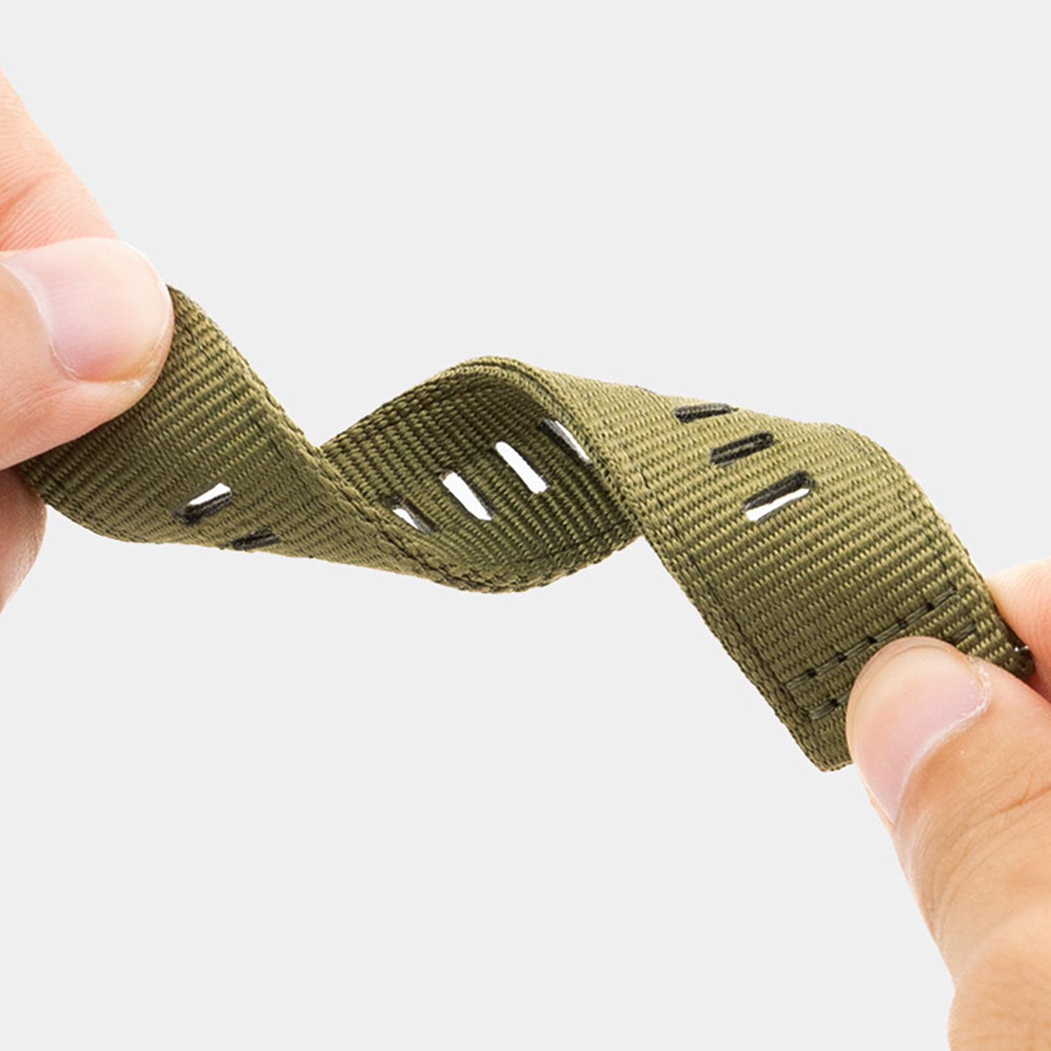 Dłonie zginające zielony pasek do zegarka. Pasek ma otwory. Dłonie trzymają pasek po obu stronach.