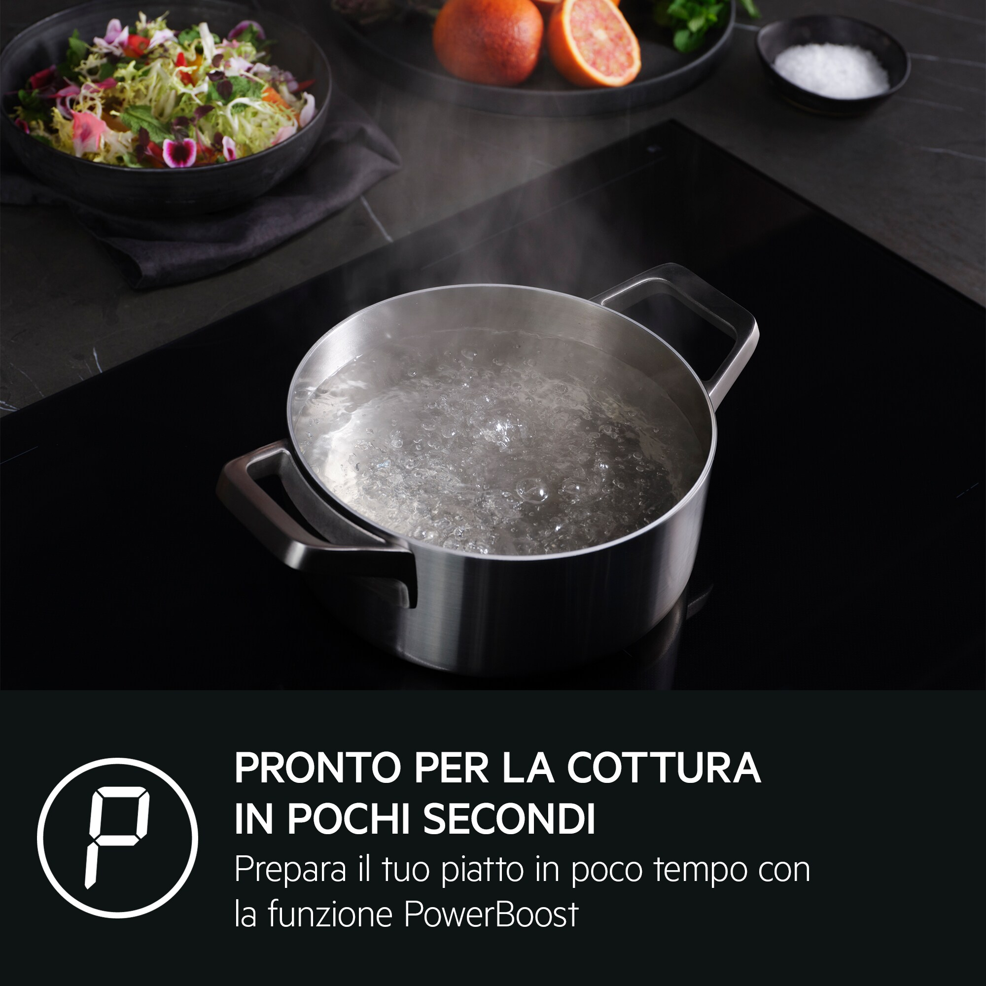 Olla con agua hirviendo en encimera negra. Ensaladera, cítricos y salero visibles.