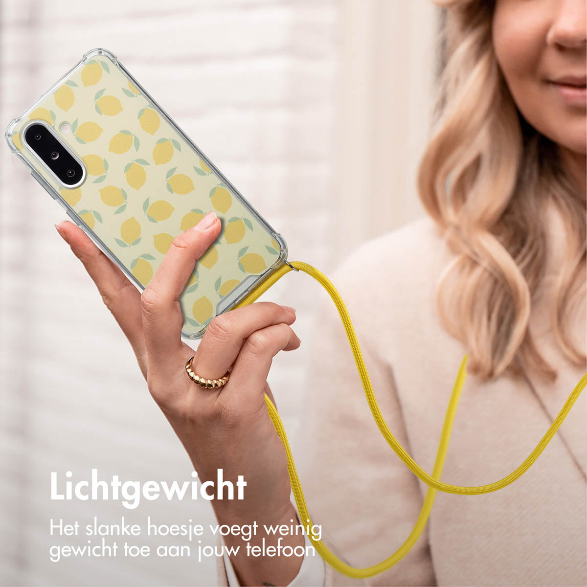 Vrouw die een telefoon met een citroenhoesje vasthoudt. De telefoon hangt aan een gele koord. Een ring om de vinger.