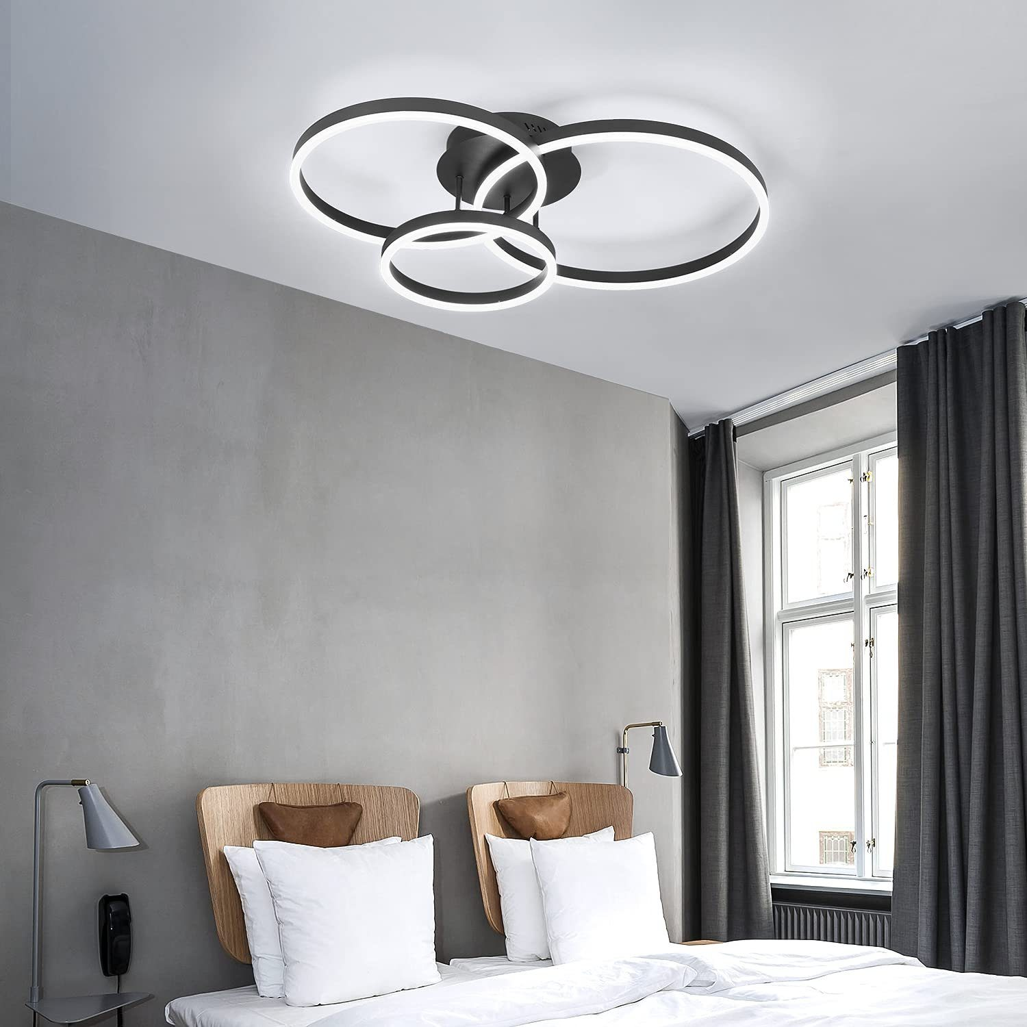 Schwarze Deckenleuchte mit ineinandergreifenden Ringen. Der Raum hat ein Bett, Lampen und Vorhänge.