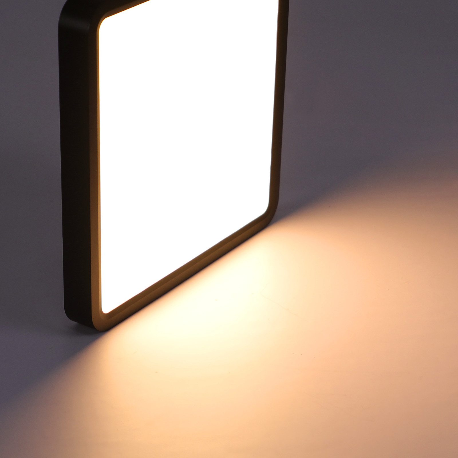 Una lámpara LED cuadrada sobre un fondo gris que proyecta una luz cálida hacia el suelo.