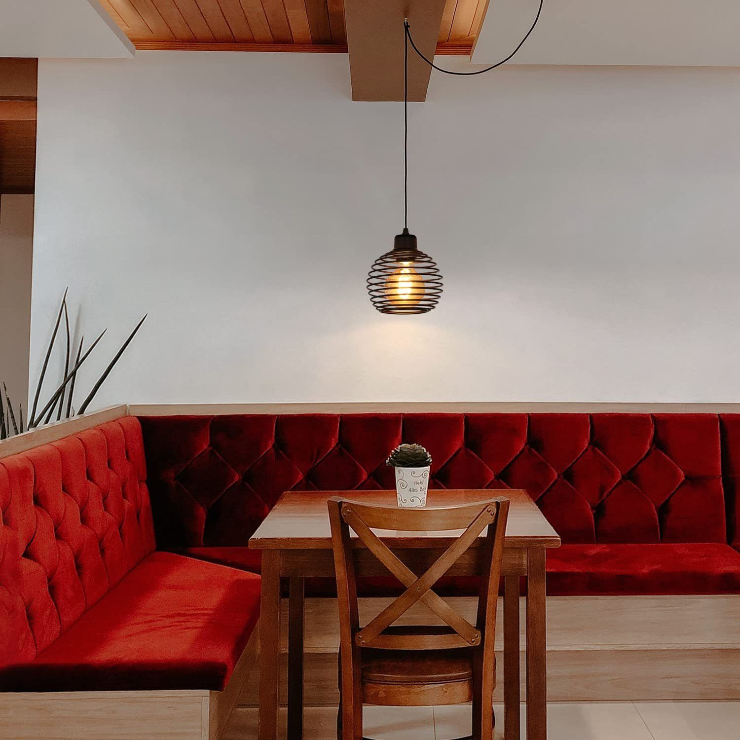 Ustawienie restauracji z czerwoną kabiną, drewnianym stołem i czarną lampą wiszącą z drucianą klatką.