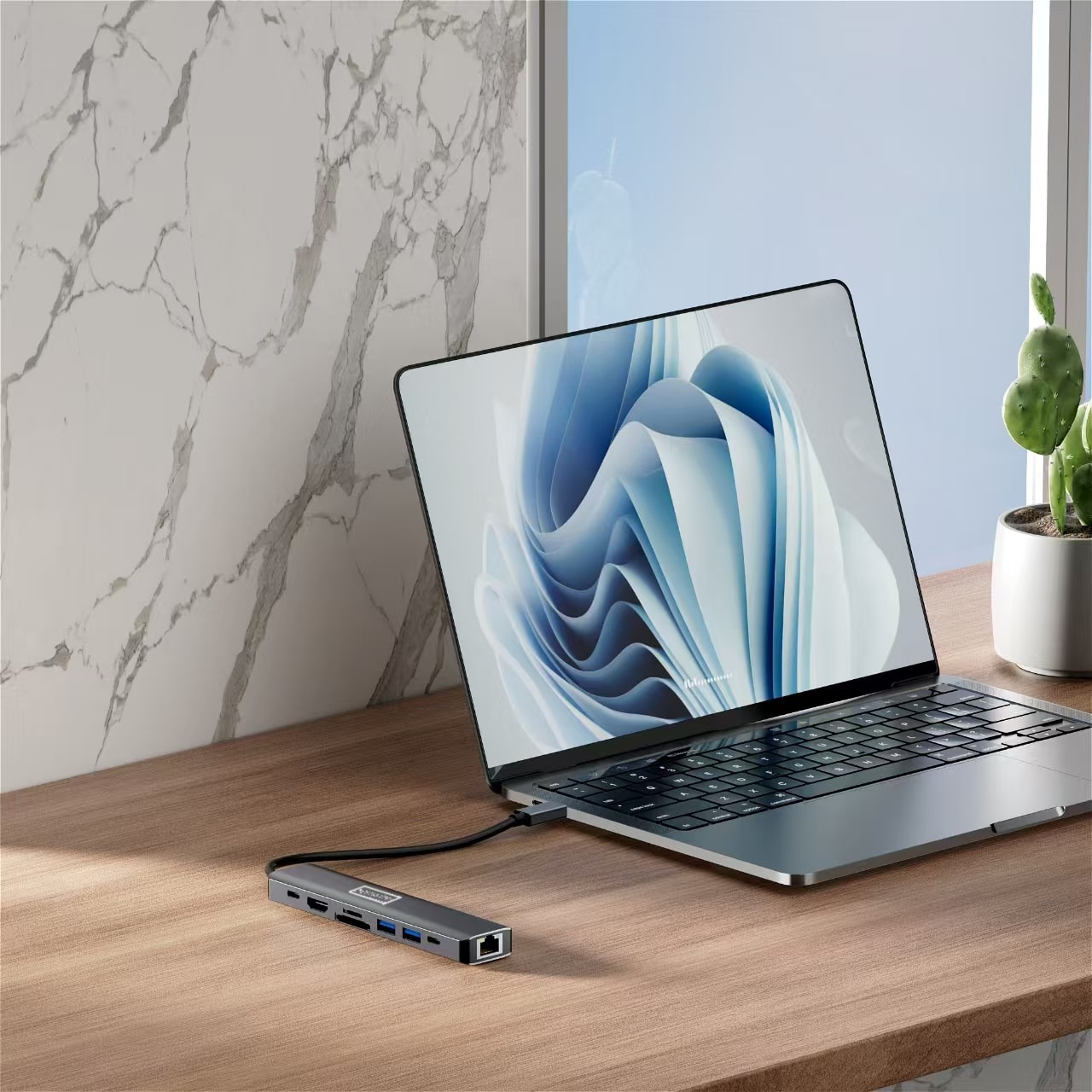 Hub USB-C podłączony do laptopa na drewnianym biurku, z oknem i marmurową ścianą.