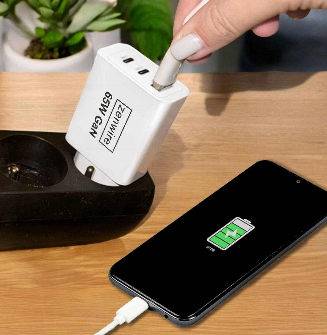 Biała ładowarka podłączona do czarnego gniazdka. Telefon ładujący się z zieloną ikoną ładowania.