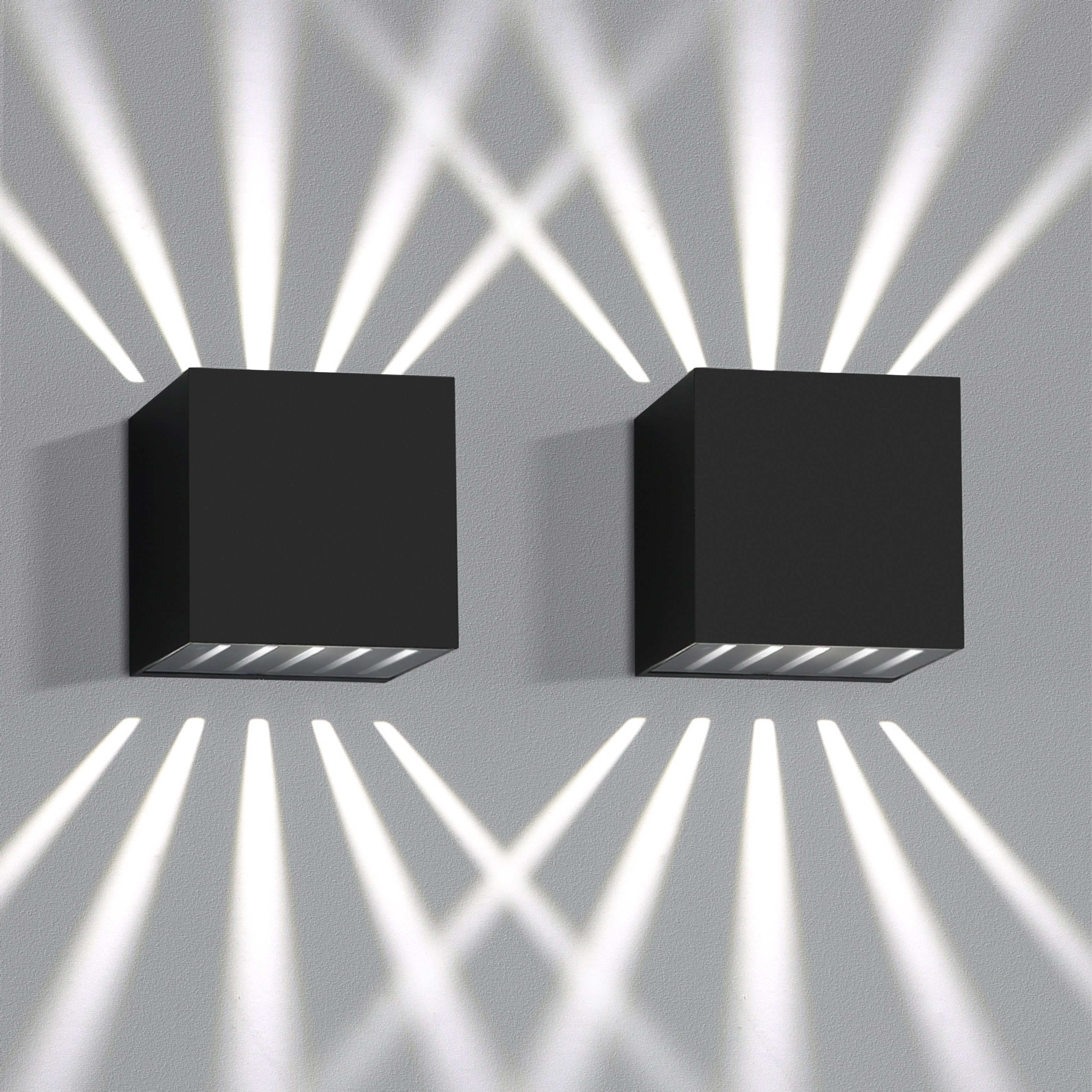 Dos lámparas cuadradas negras en una pared gris. Emiten haces de luz.