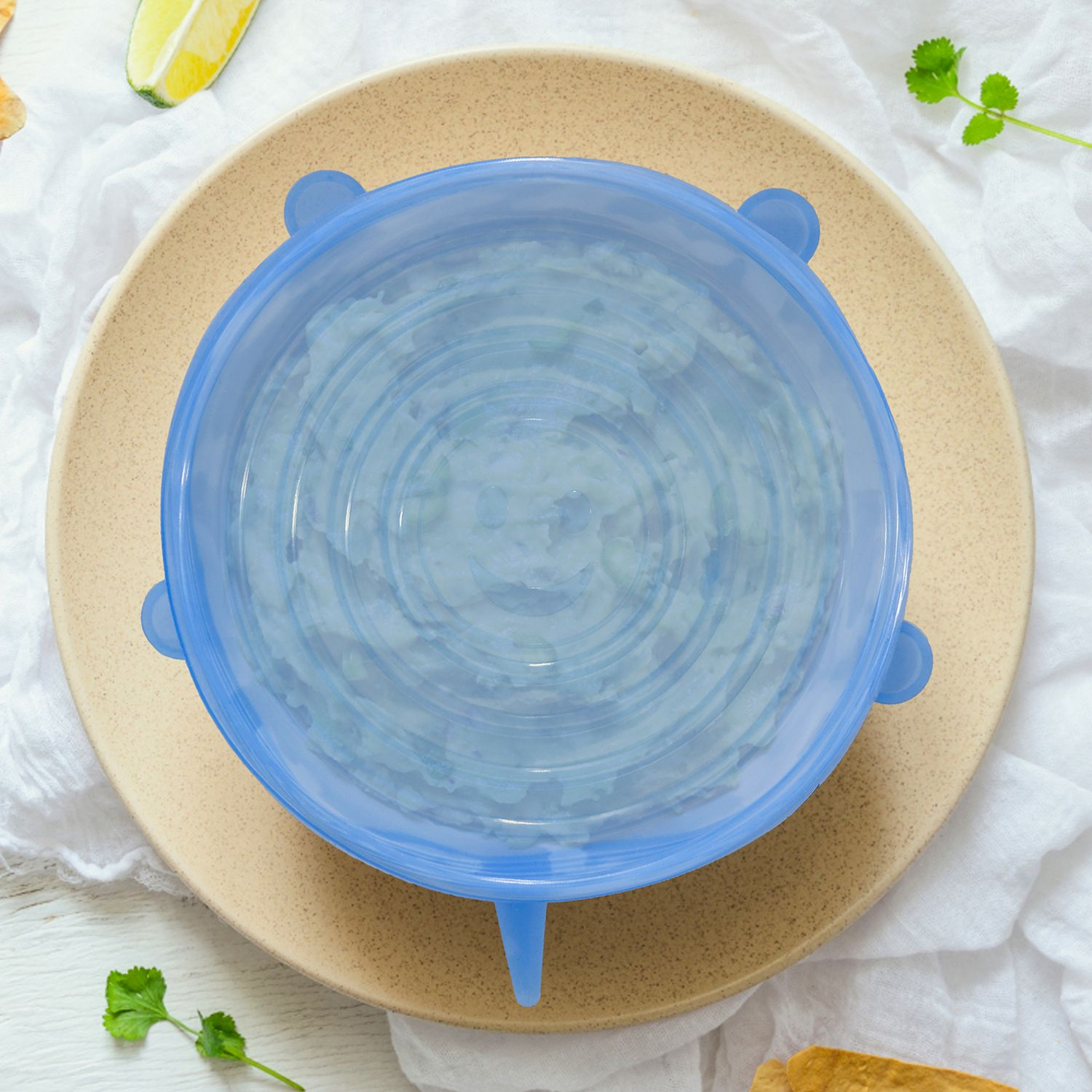 Eine blaue Schüsselhaube auf einem Teller mit Essen. Limette und Petersilie liegen auf dem weißen Tuch im Hintergrund.