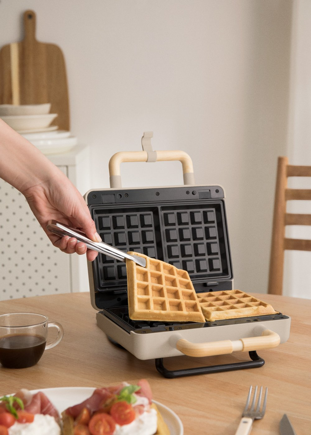 Una mano usando pinzas para sacar un gofre de una gofrera, con mango de madera.