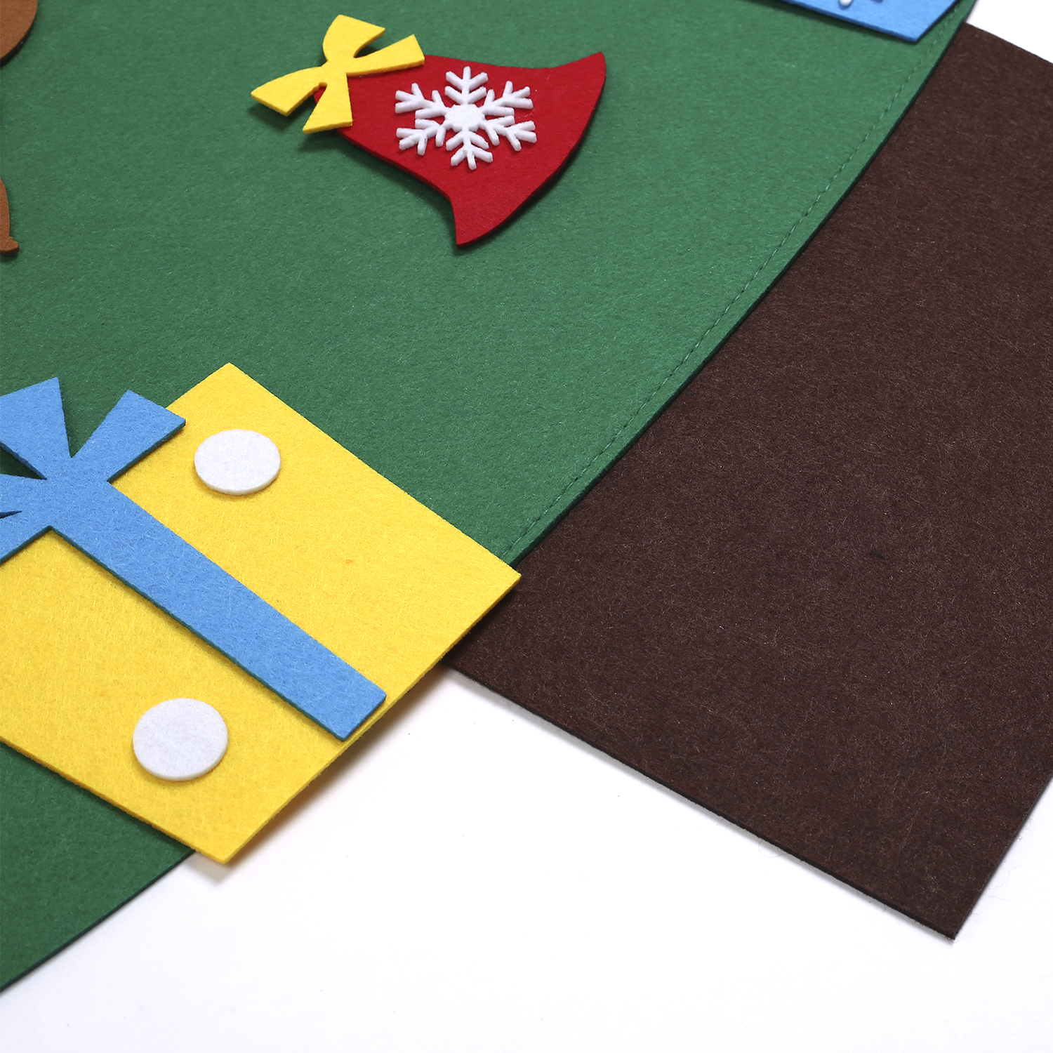 Primer plano de una decoración navideña de fieltro: regalo amarillo, copo de nieve, sombrero rojo y fondo marrón.