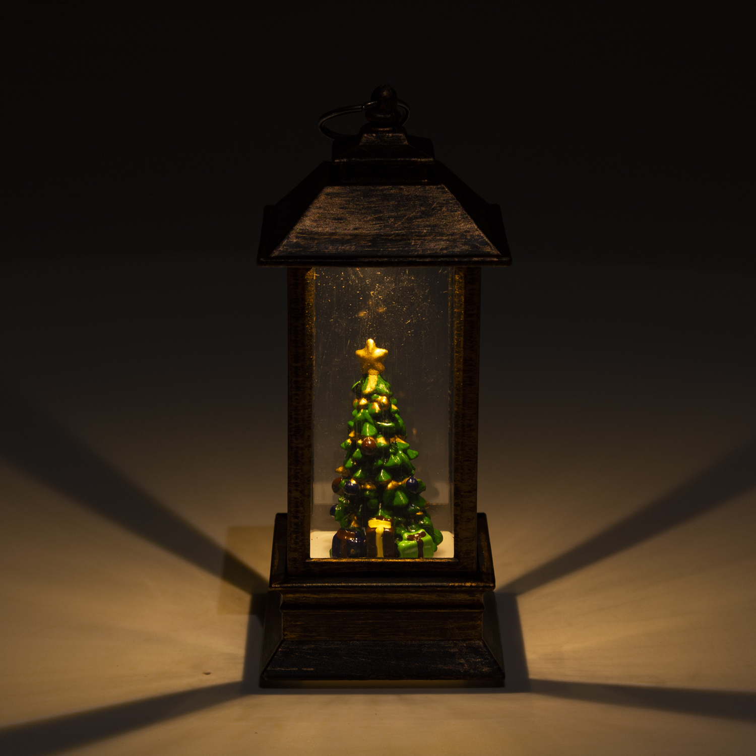 Beleuchtete Laterne mit Weihnachtsbaum im Inneren, die auf einer weißen Oberfläche vor dunklem Hintergrund steht.