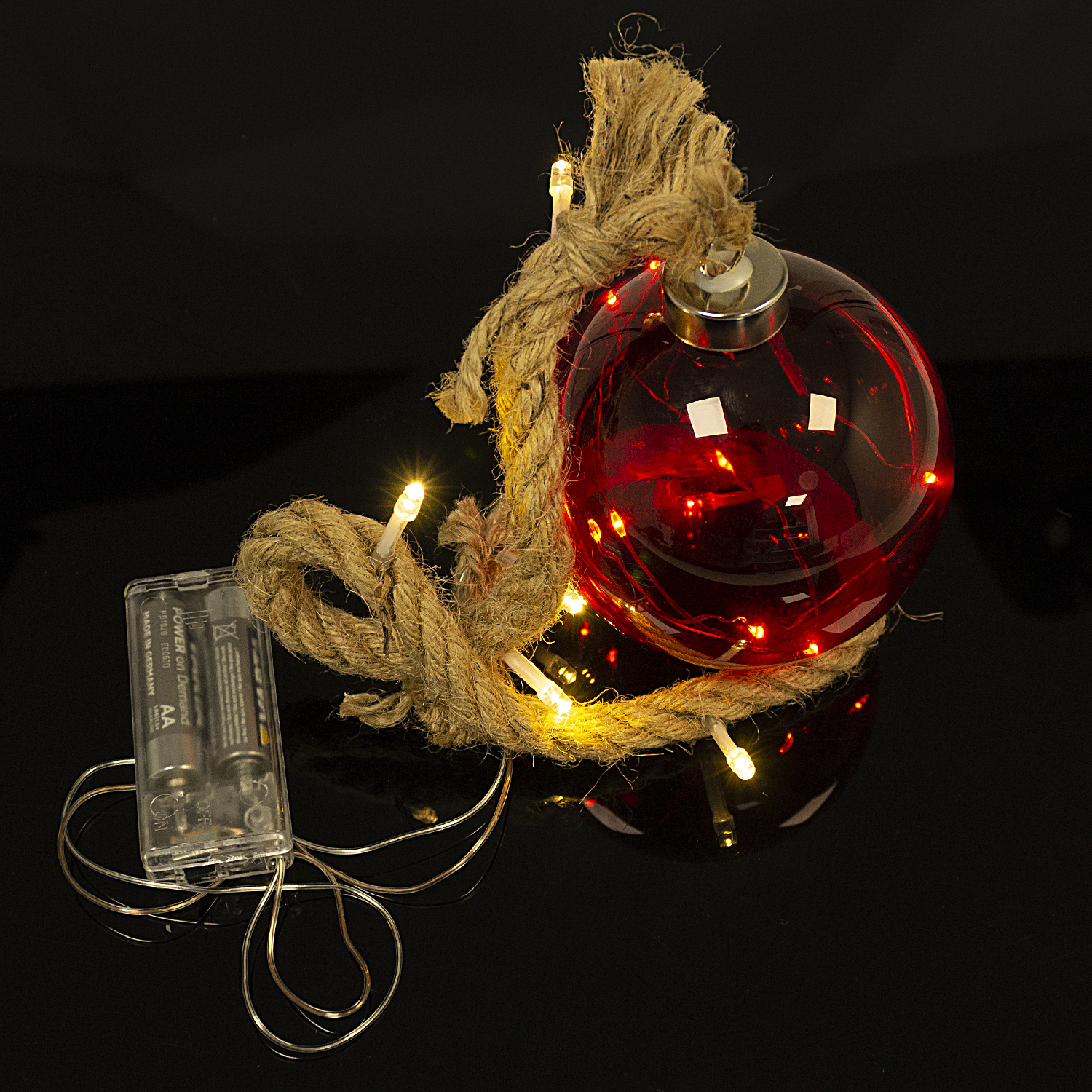 Ornamento in vetro rosso con luci avvolte in corda, con batterie su superficie nera.