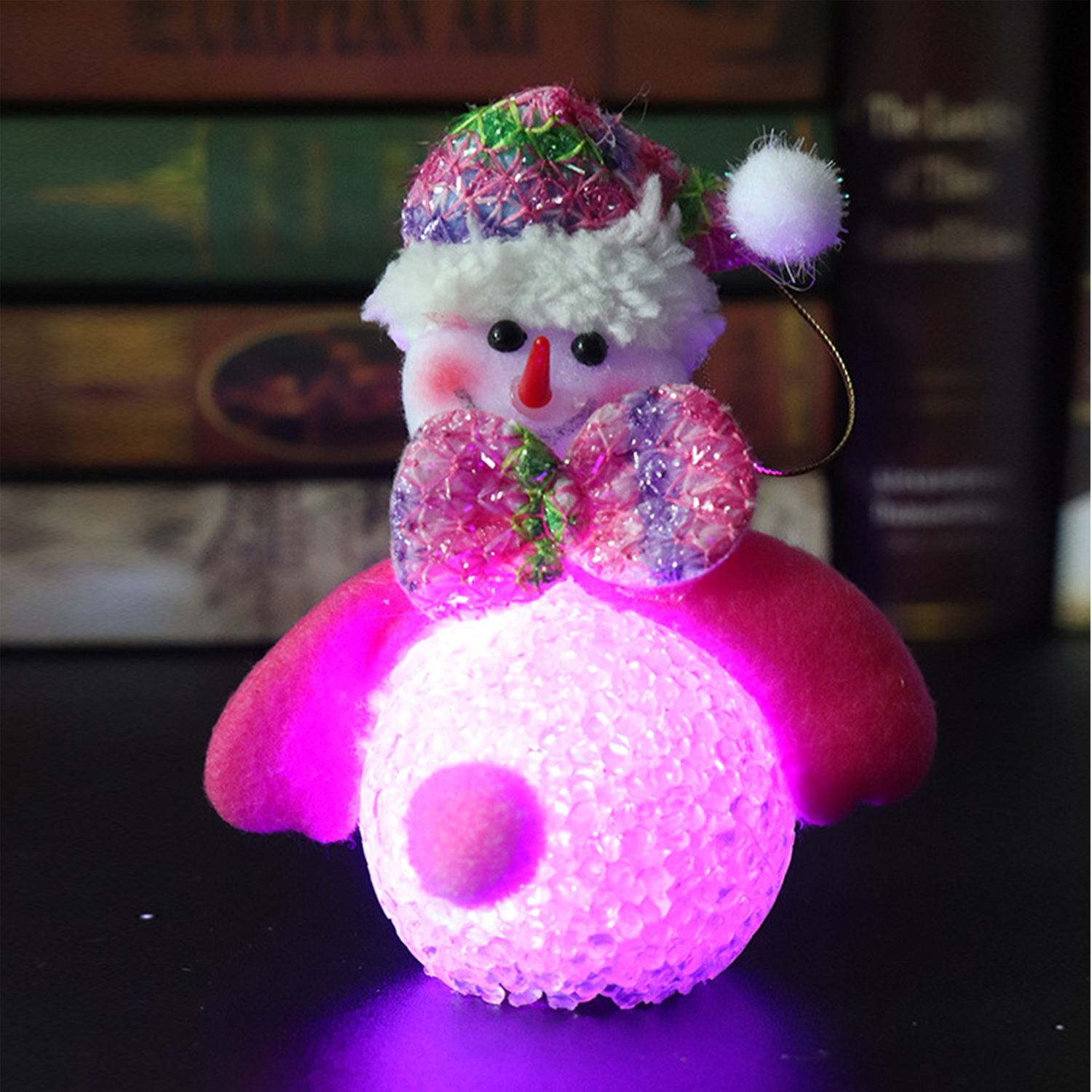 Ornamento a pupazzo di neve con fiocco rosa e palla luminosa. Libri sullo sfondo.