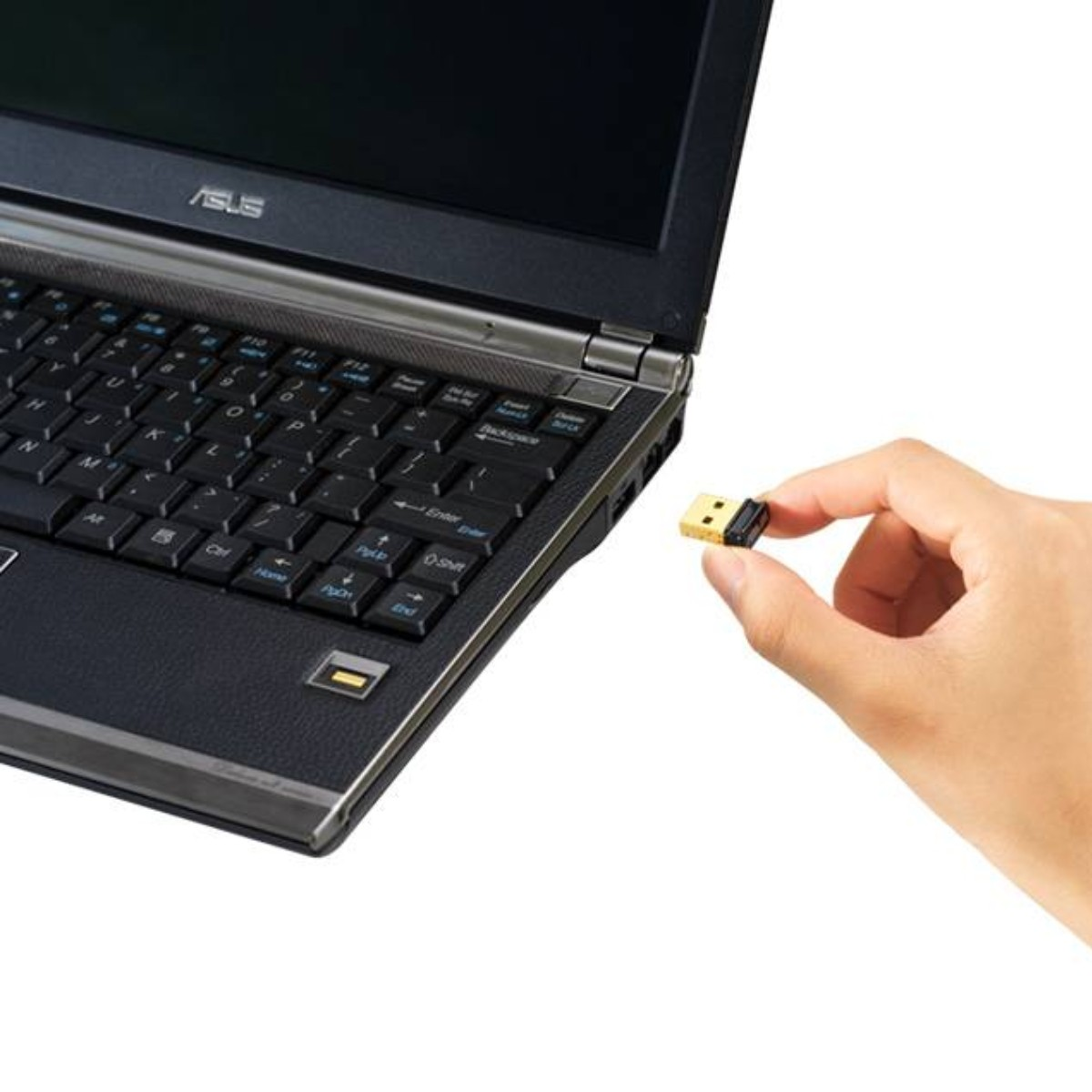 Ręka trzymająca mały odbiornik USB obok laptopa. Laptop jest otwarty, z czarną klawiaturą i szarą ramką.