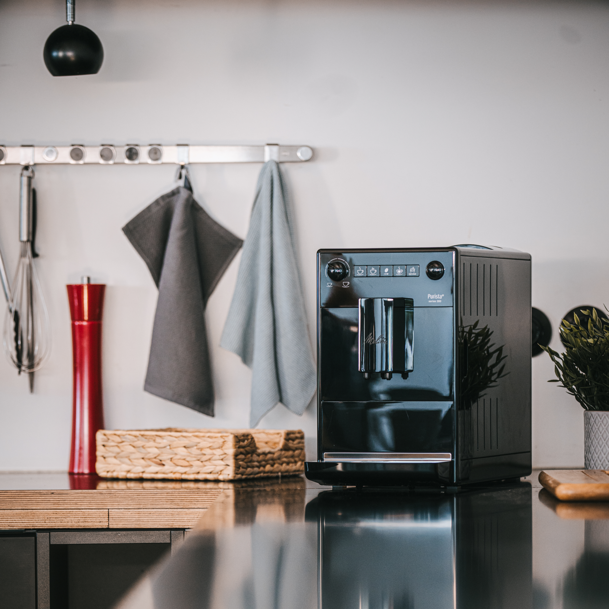 Czarny ekspres do kawy na blacie kuchennym. Akcesoria kuchenne i roślina w tle.