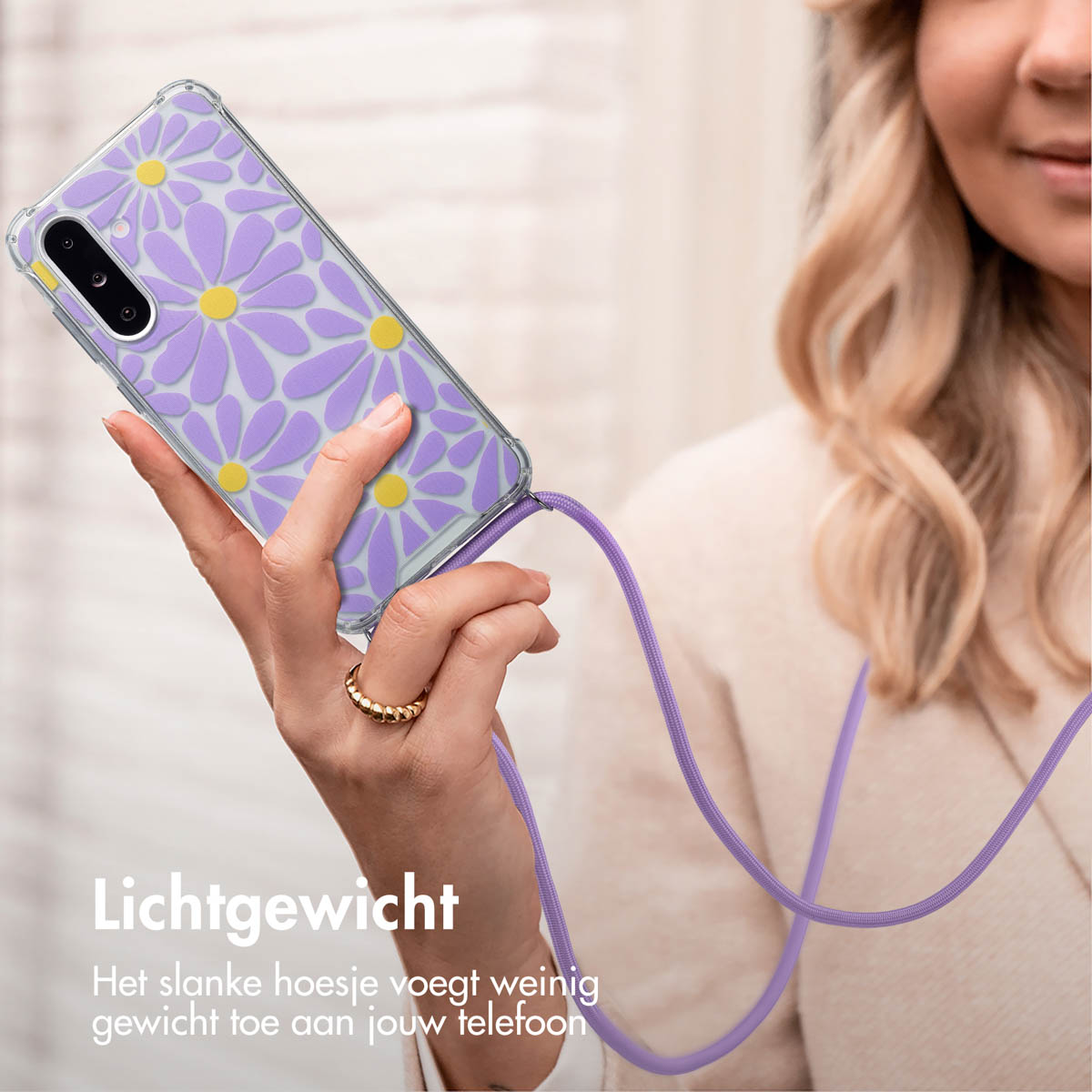 Vrouw houdt telefoonhoes met paarse madeliefjes vast, ring om vinger, wazige achtergrond.