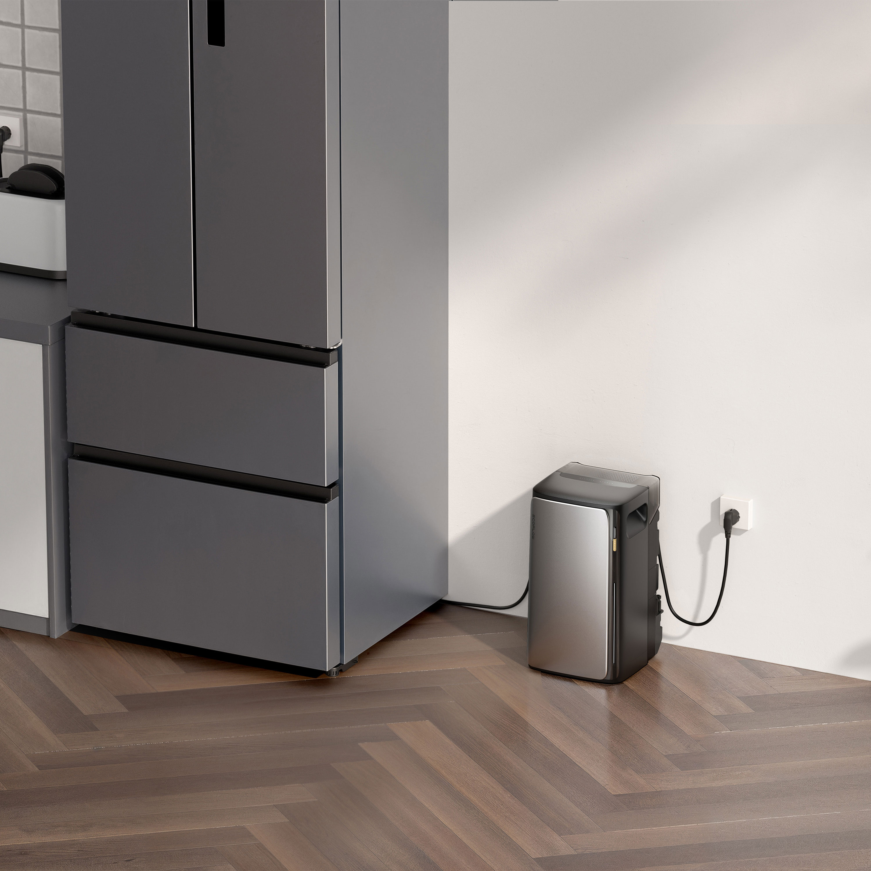 A kitchen with a gray refrigerator and a small black and silver appliance plugged into a wall outlet.