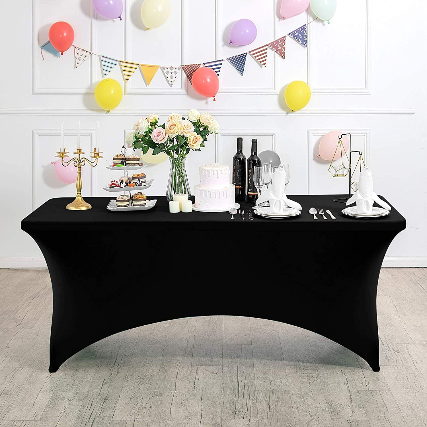 Un mantel negro cubre una mesa para una fiesta. Globos y decoraciones en el fondo.