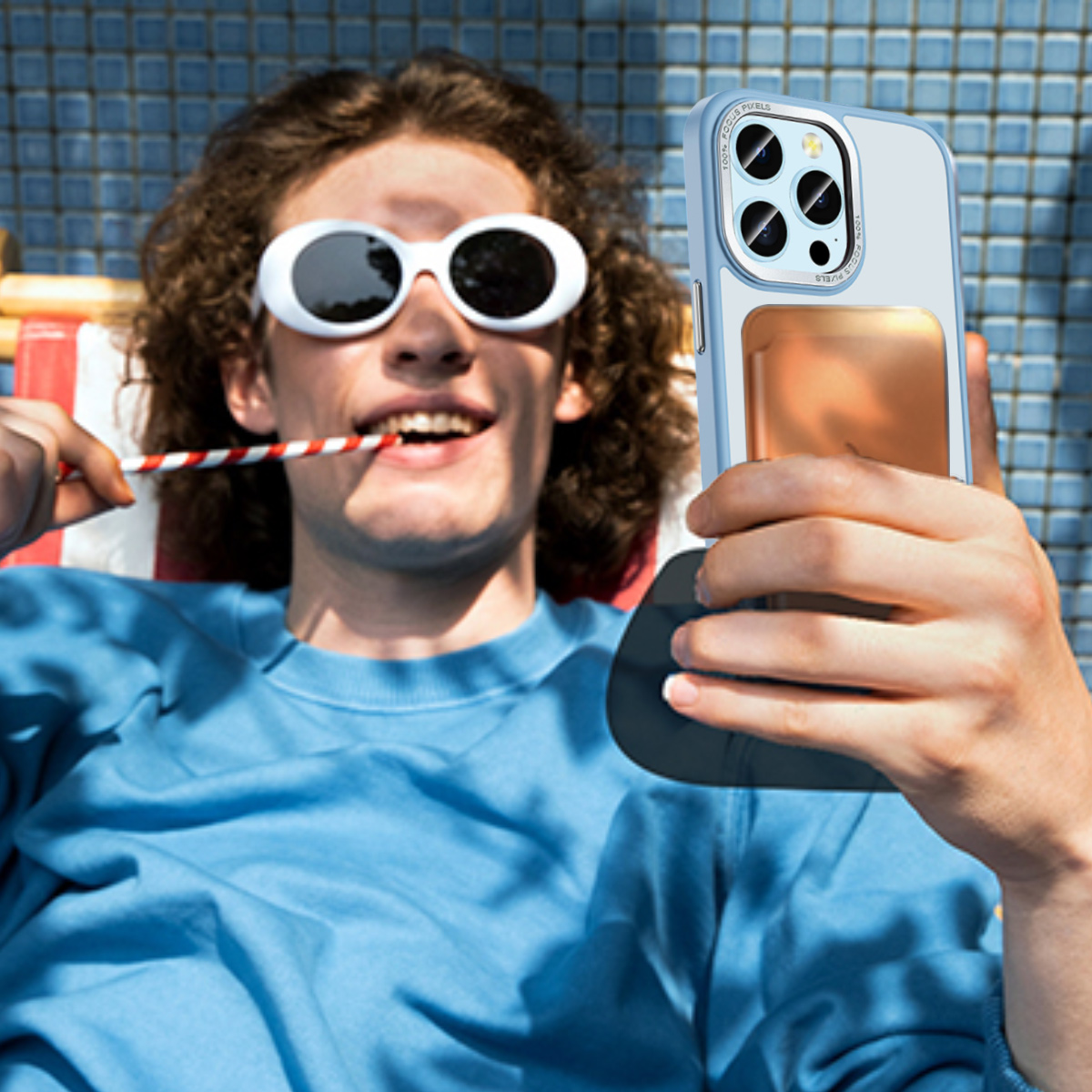 Ein Mann liegt, trägt Sonnenbrille und hält ein Handy mit Hülle für ein Selfie.