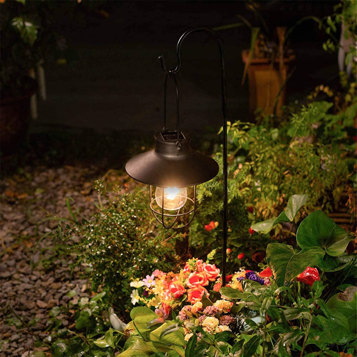 Schwarze Gartenlaterne mit Solarpanel, platziert in einem Garten mit Blumen.