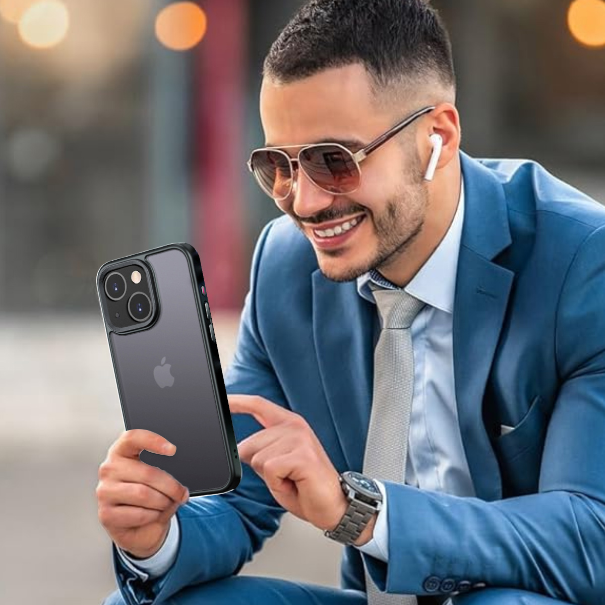 Ein Mann hält ein Telefon mit Hülle, lächelt. Er trägt Sonnenbrille, Anzug und Ohrhörer.