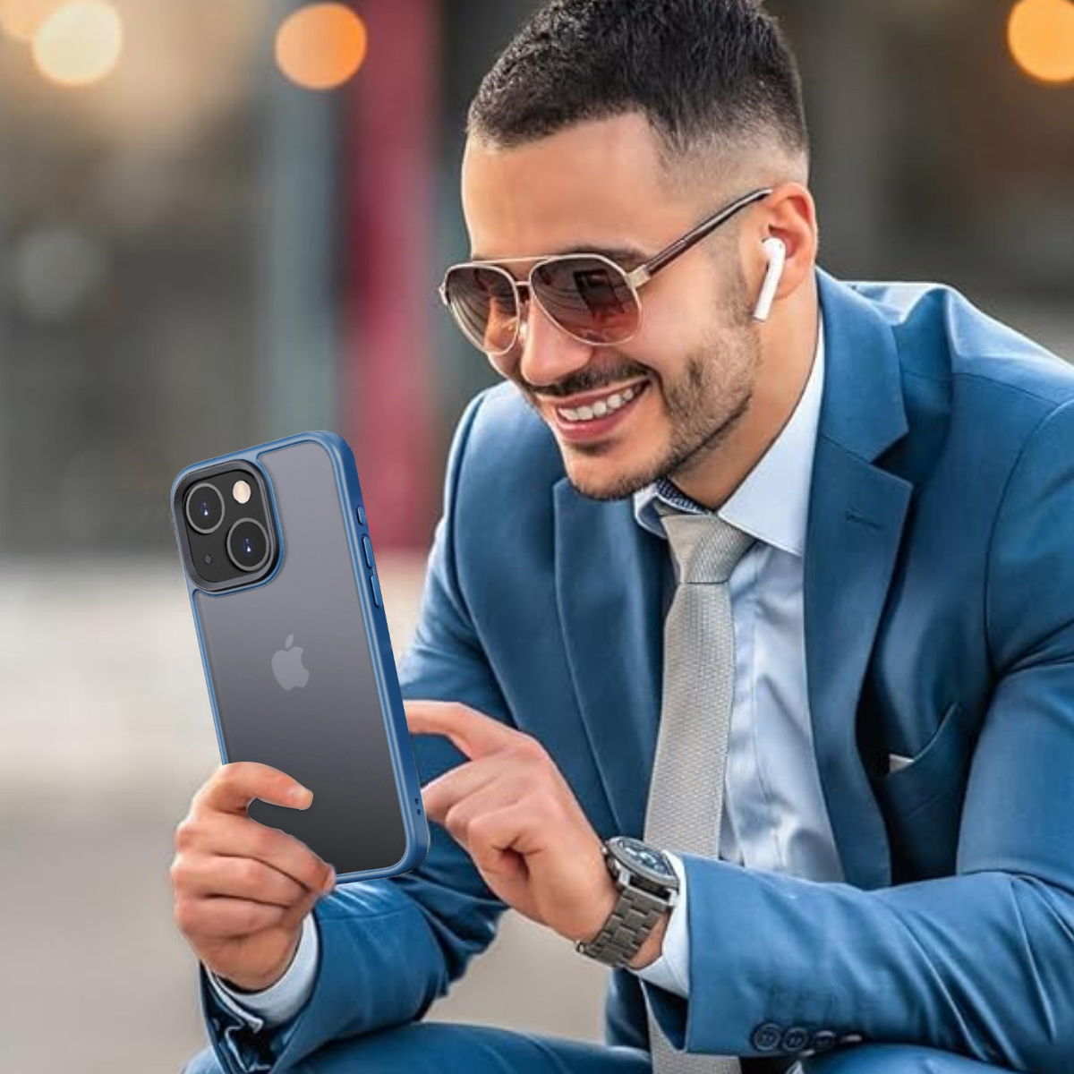 Ein Mann hält ein Telefon in einer blauen Hülle und lächelt. Er trägt Anzug, Krawatte, Sonnenbrille und Ohrhörer.