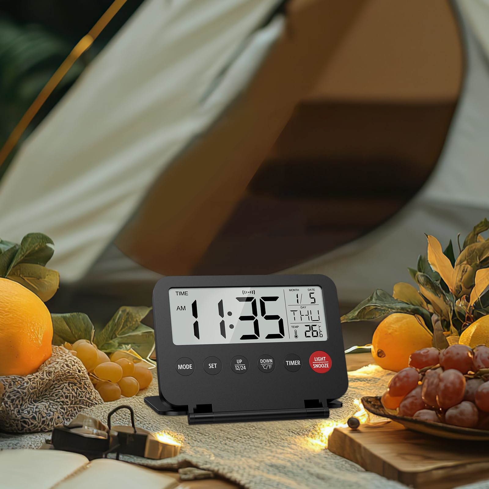 Eine schwarze Digitaluhr, die die Uhrzeit anzeigt, mit Obst und einem Zelt im Hintergrund.