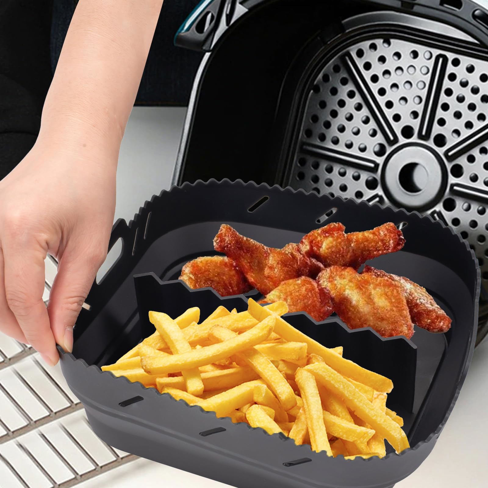 Pommes und Hähnchenflügel in einem schwarzen Airfryer-Korb. Hand hält den Korb.