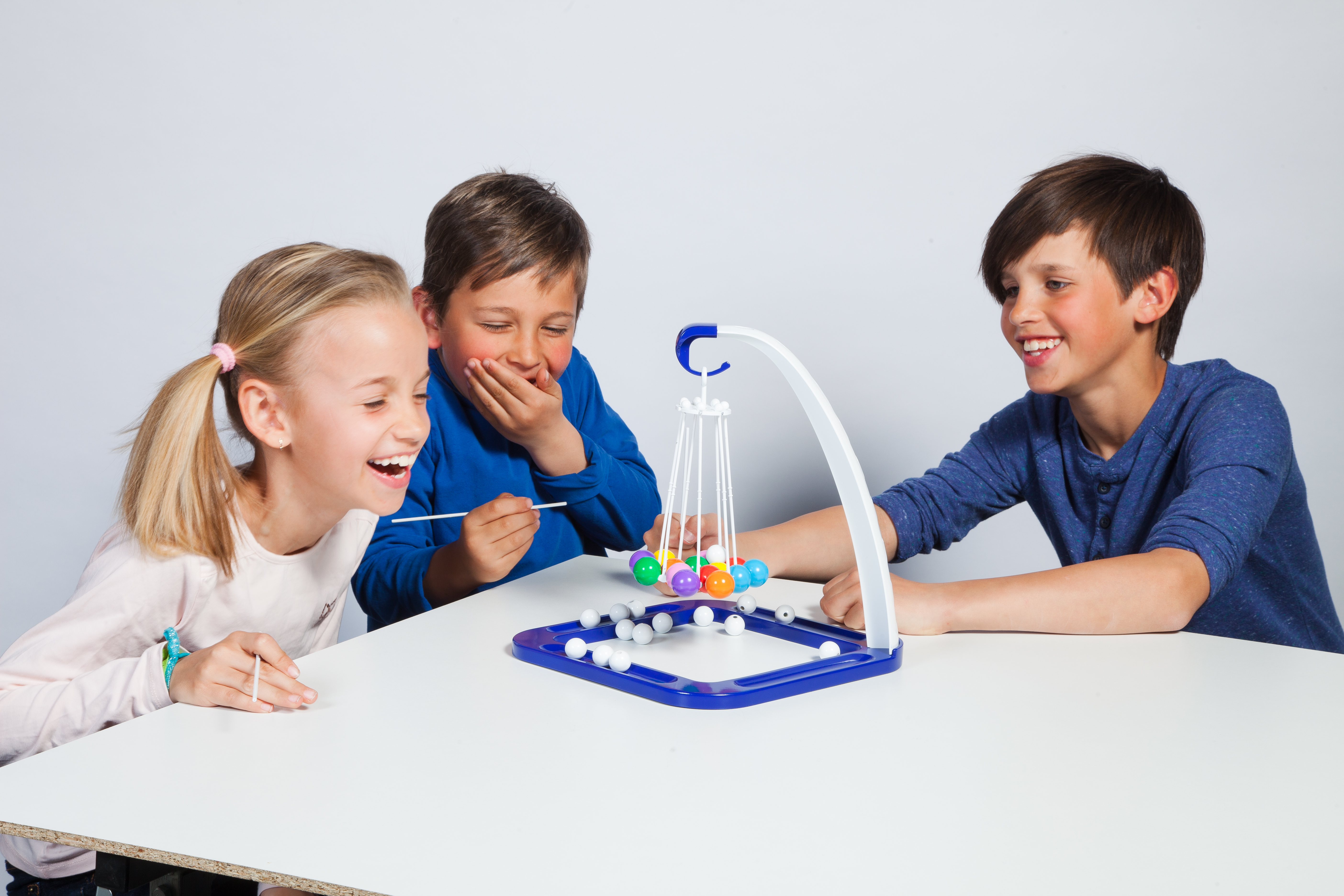 Tre bambini giocano a un gioco con la palla con palline colorate e un tavolo bianco. Ridono.