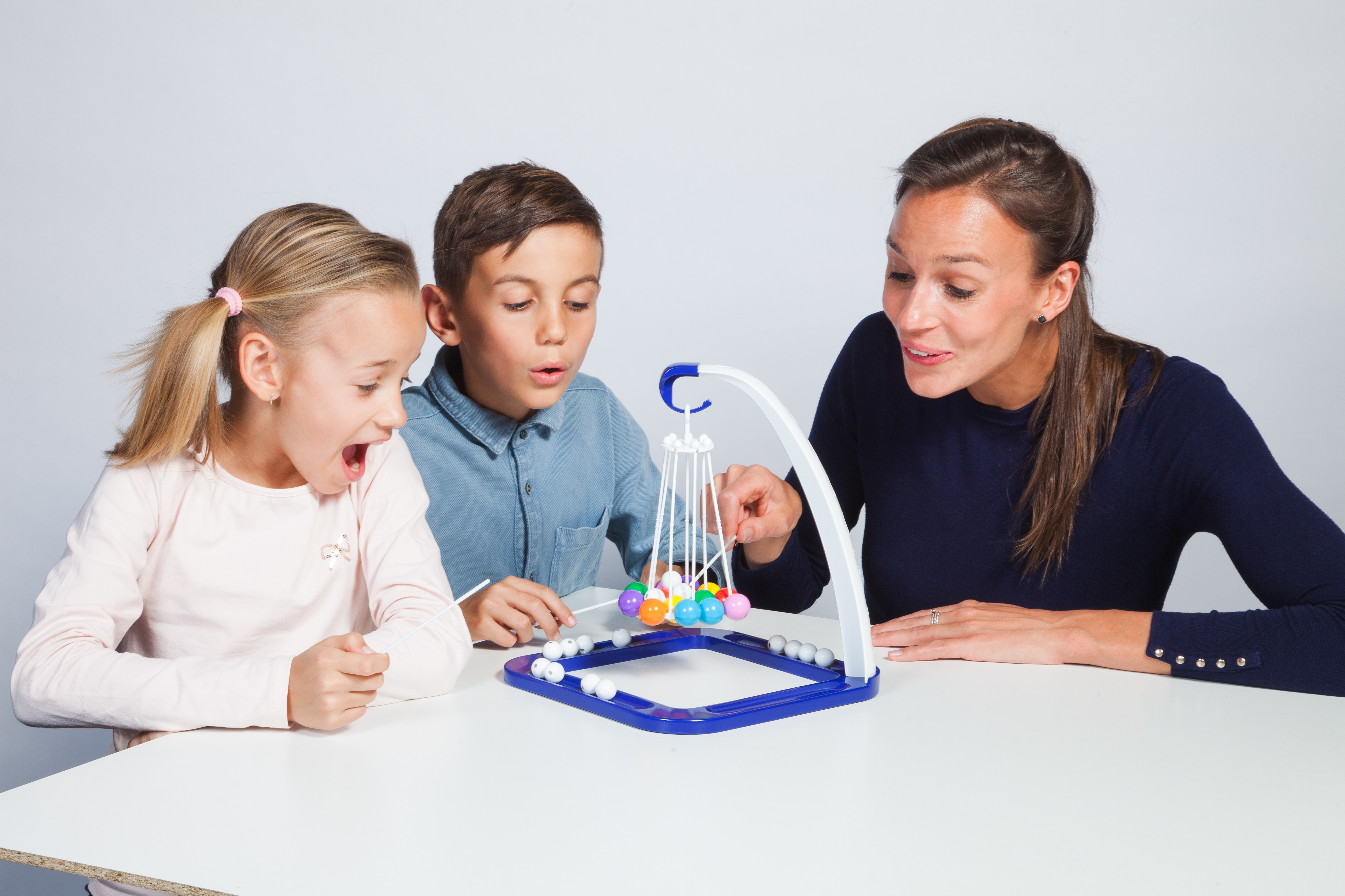 Una donna e due bambini giocano a un gioco con la palla con palline colorate su un tavolo bianco. Sono eccitati.