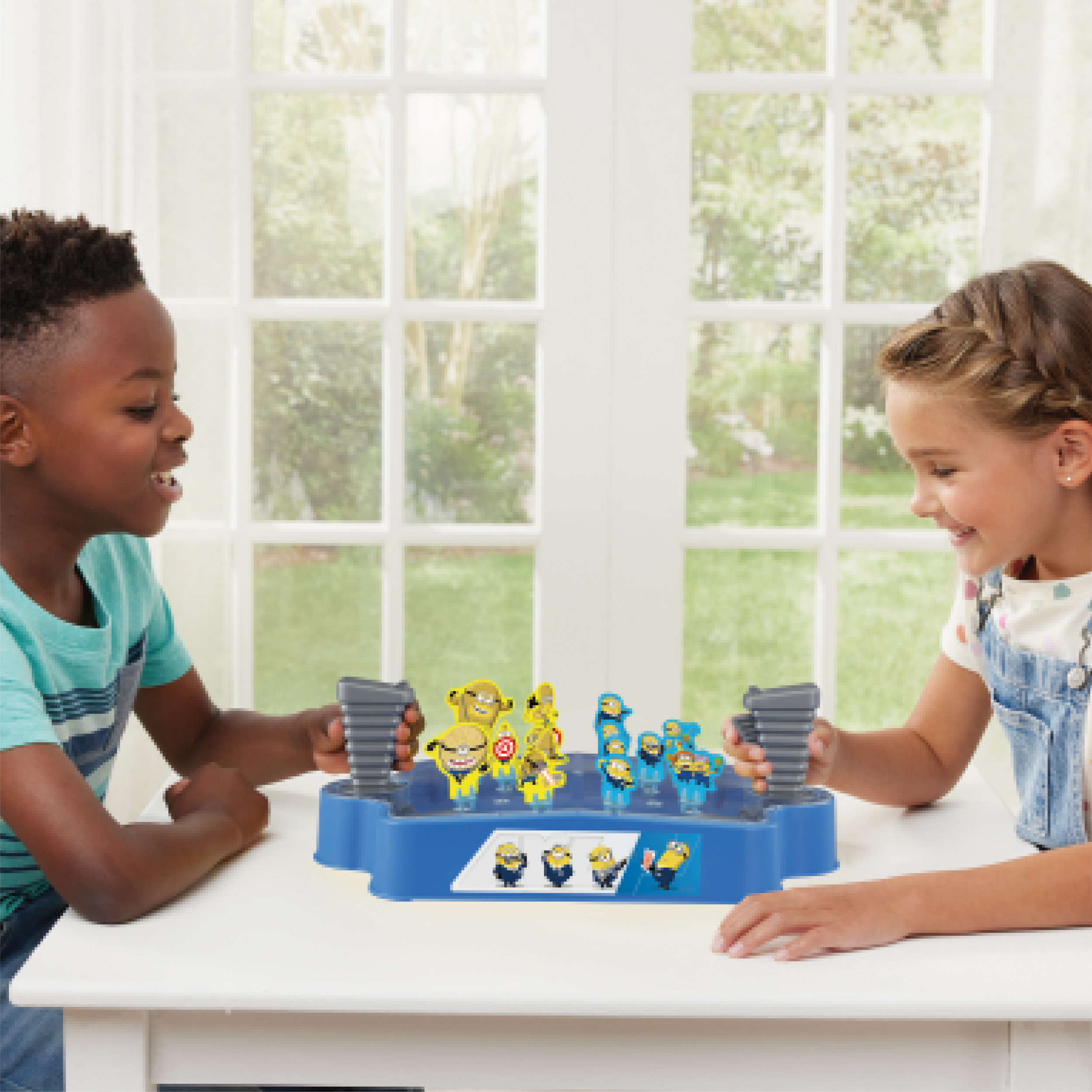 Zwei Kinder spielen ein Minions-Spiel. Das Spiel ist blau mit Minion-Figuren, auf einem weißen Tisch.