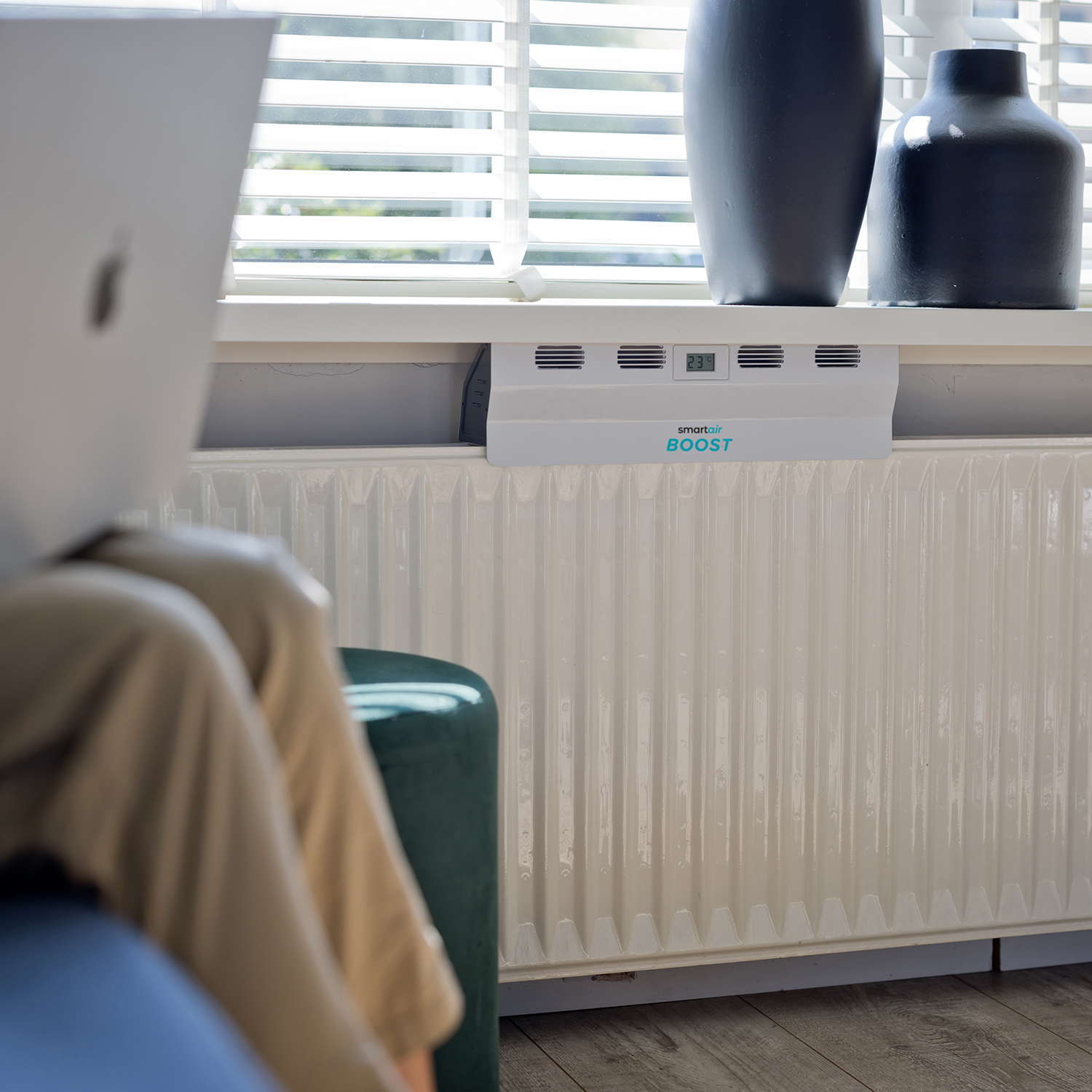 Persoon die een laptop gebruikt in de buurt van een radiator met een smart air boost-apparaat.