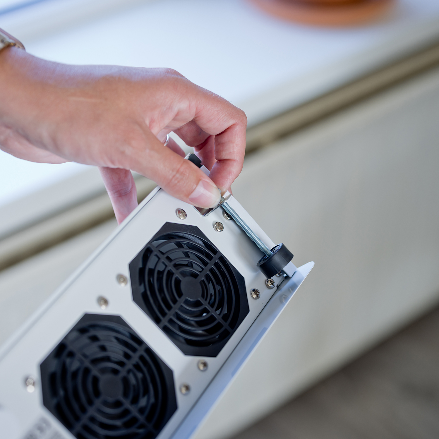 Hand die een schroef in een apparaat met twee ventilatoren draait. Lichte achtergrond.