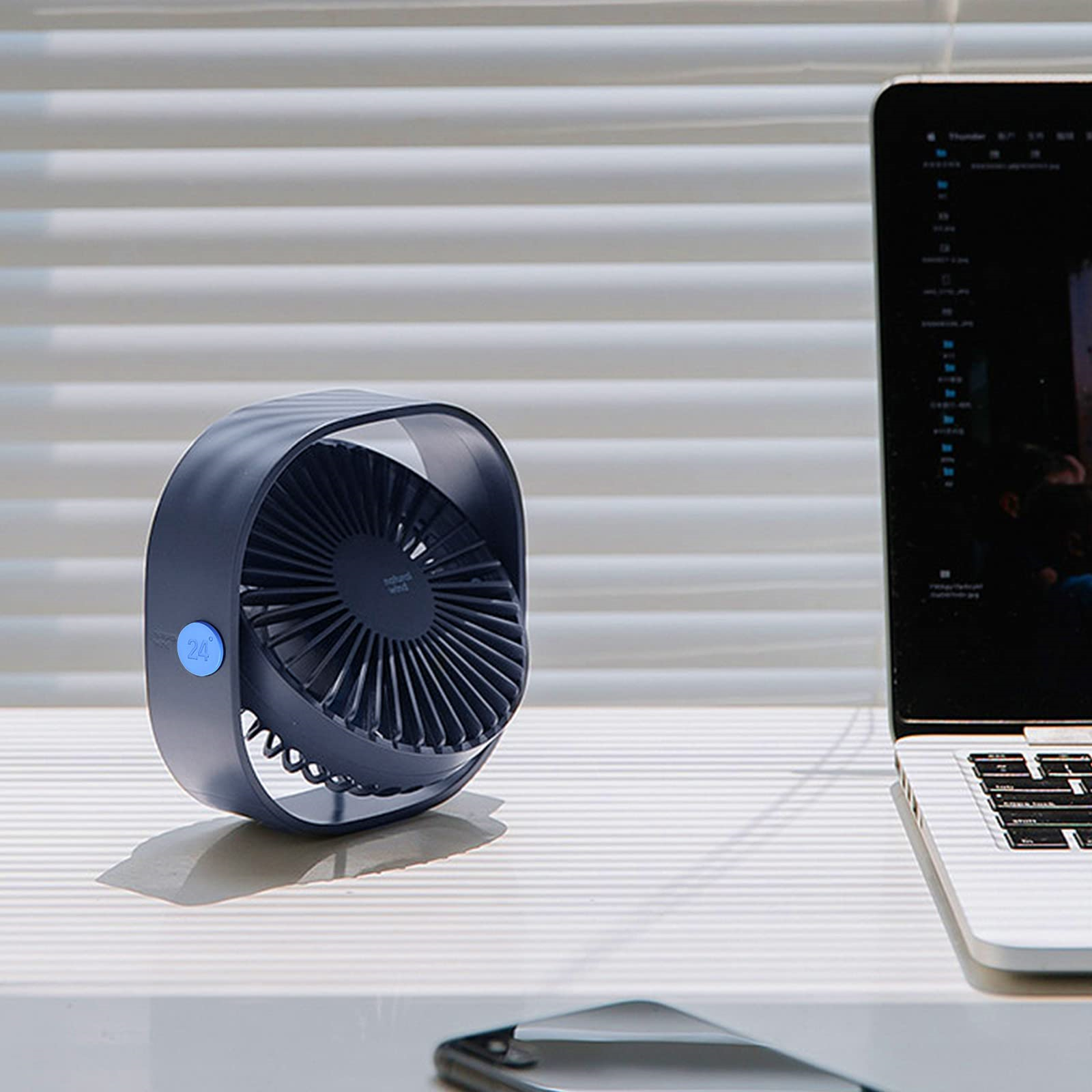 Ein kleiner blauer Ventilator in der Nähe eines Laptops auf einem weißen Schreibtisch. Der Ventilator läuft.