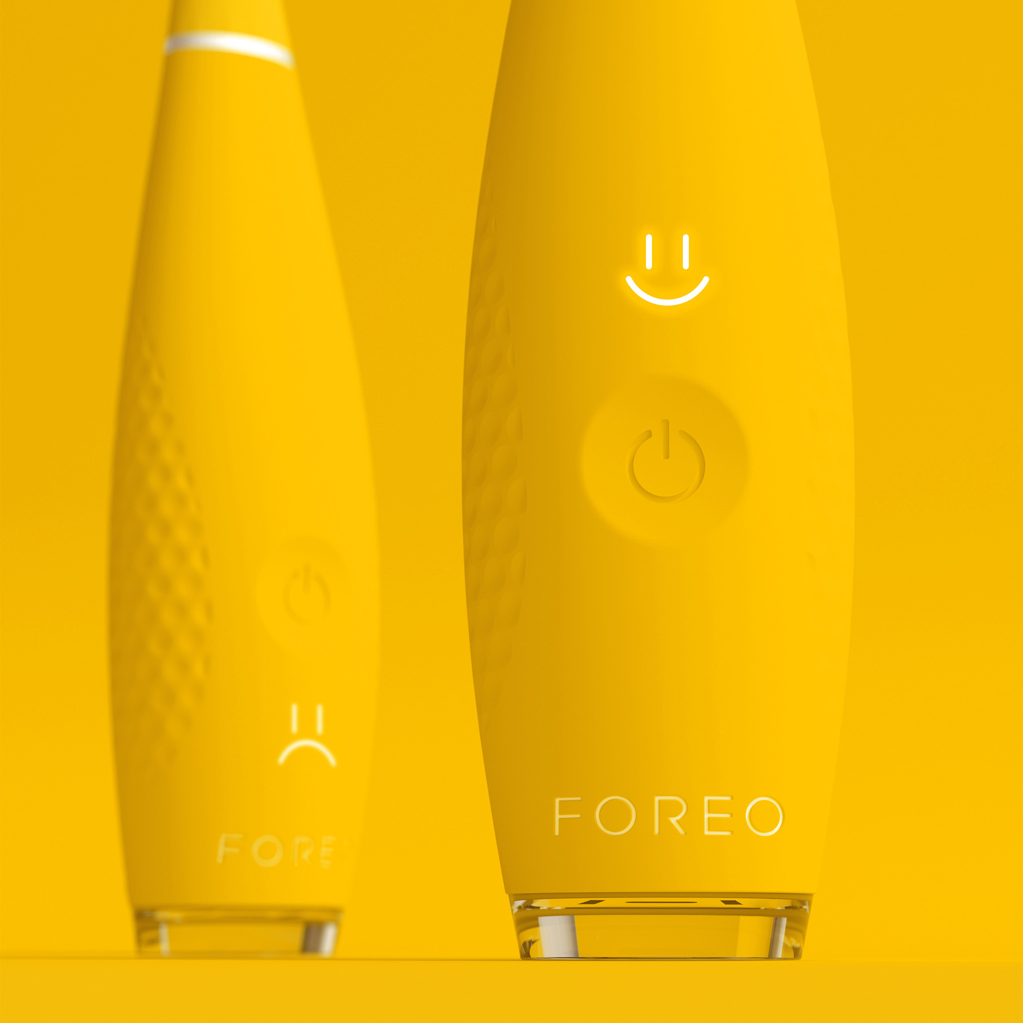 Dos cepillos de dientes Foreo amarillos. Uno tiene una carita sonriente, otro triste.