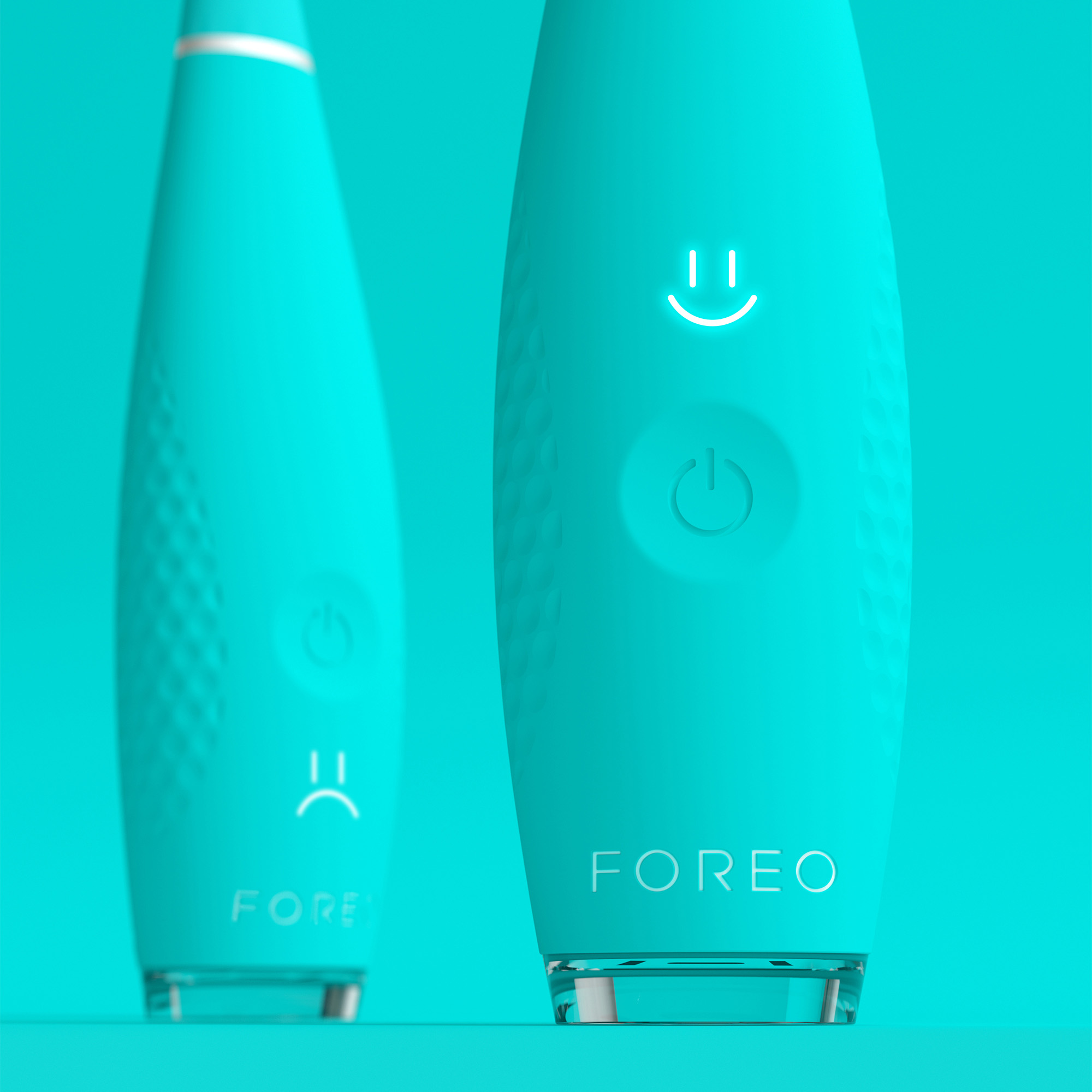 Dos dispositivos Foreo turquesa, uno sonriendo y otro con cara triste.