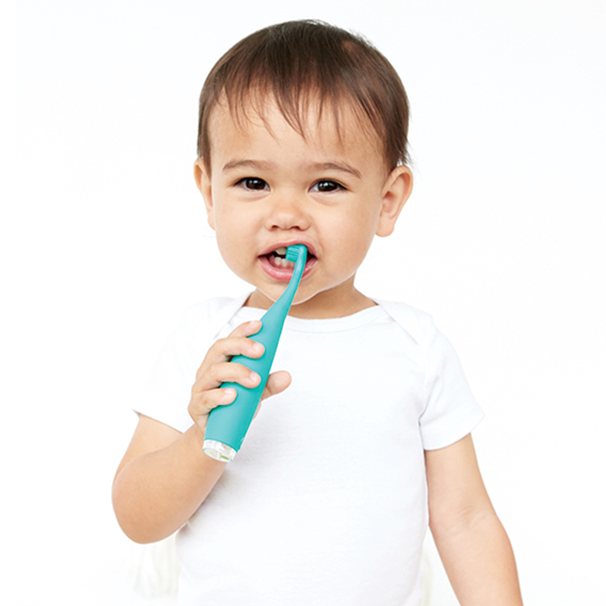 Un bambino in tutina bianca che si lava i denti con uno spazzolino verde.