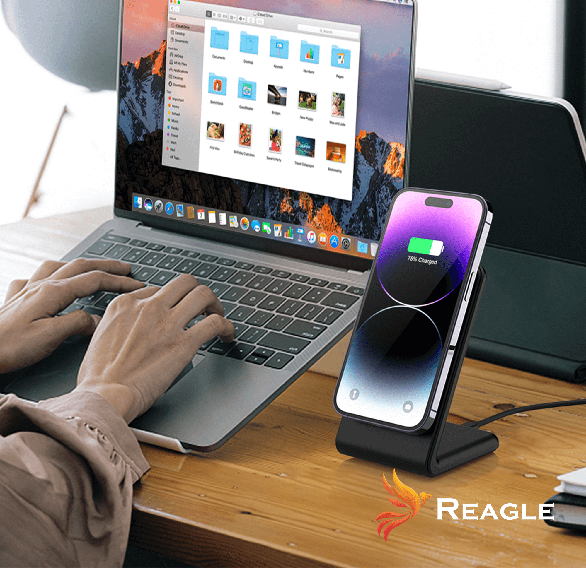 Osoba korzysta z laptopa z telefonem ładującym się na podstawce. Biurko znajduje się na pierwszym planie.