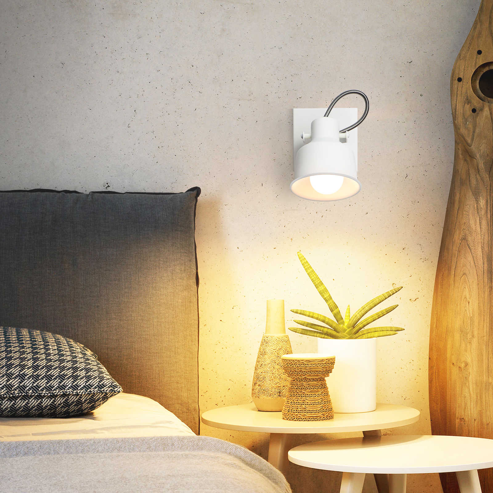 Biała lampa ścienna z regulowanym ramieniem. Stolik nocny z roślinami na pierwszym planie.
